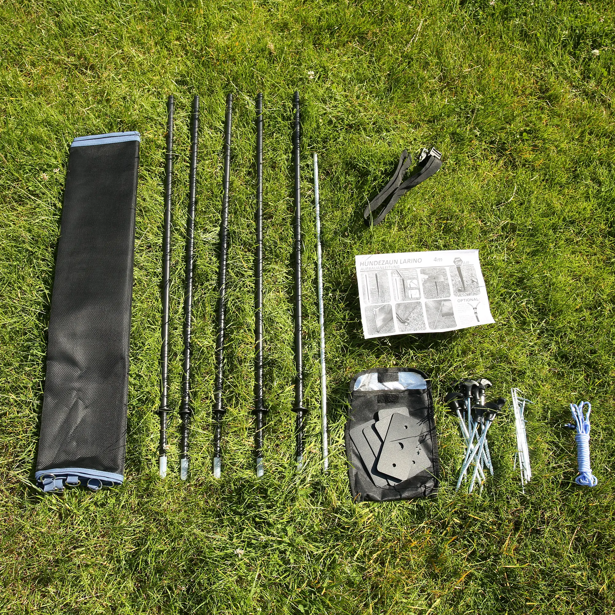 Clôture pour chien your GEAR Larino 400 démontée : poteaux, piquets, sangles, corde, sac de transport, notice et accessoires disposés sur l’herbe, idéale pour camping et jardin, extensible à volonté.