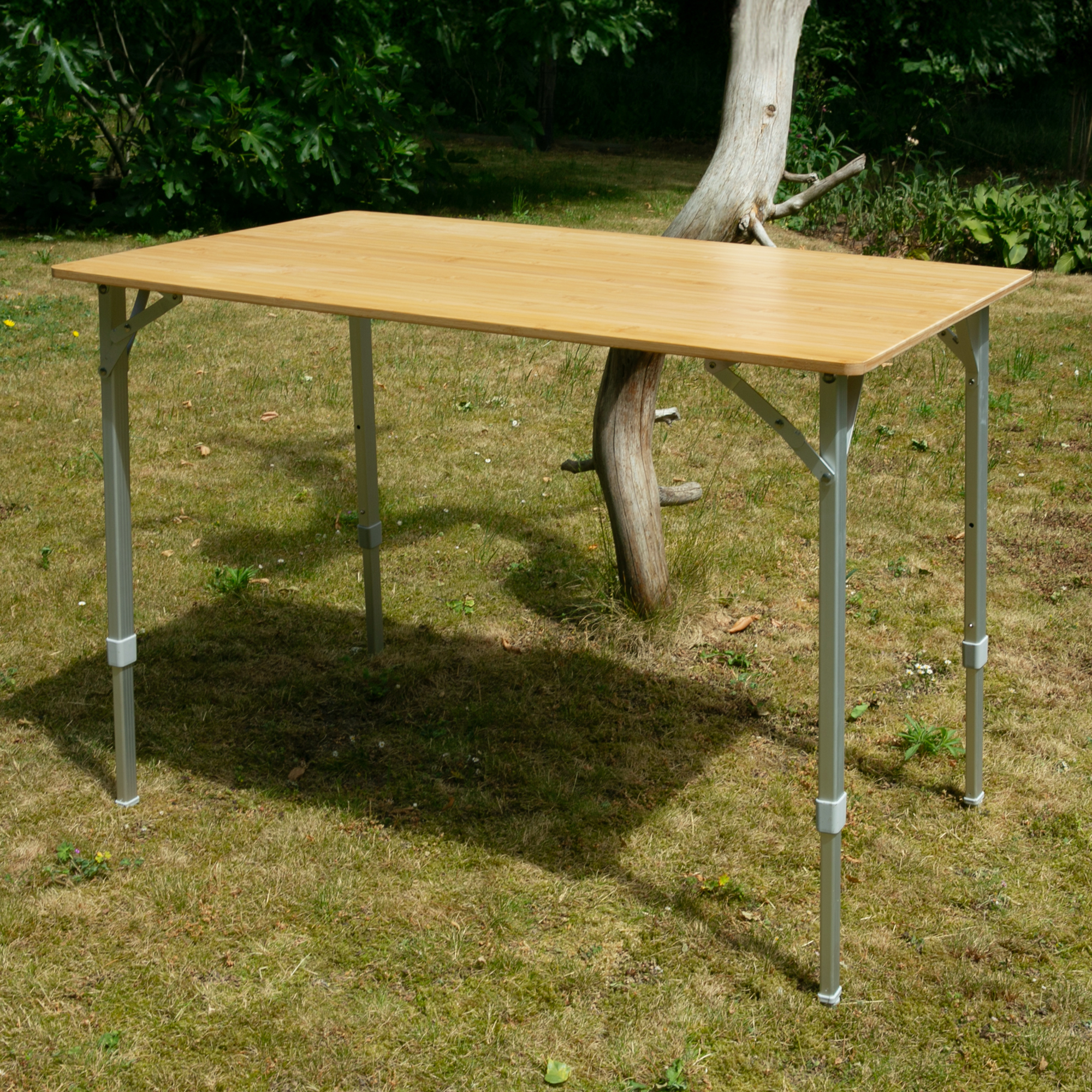 Bamboo camping table your GEAR Portofino L for 4 people, rectangular 100x60 cm, natural bamboo tabletop, foldable metal legs with three height settings, outdoor use, set up on grass.