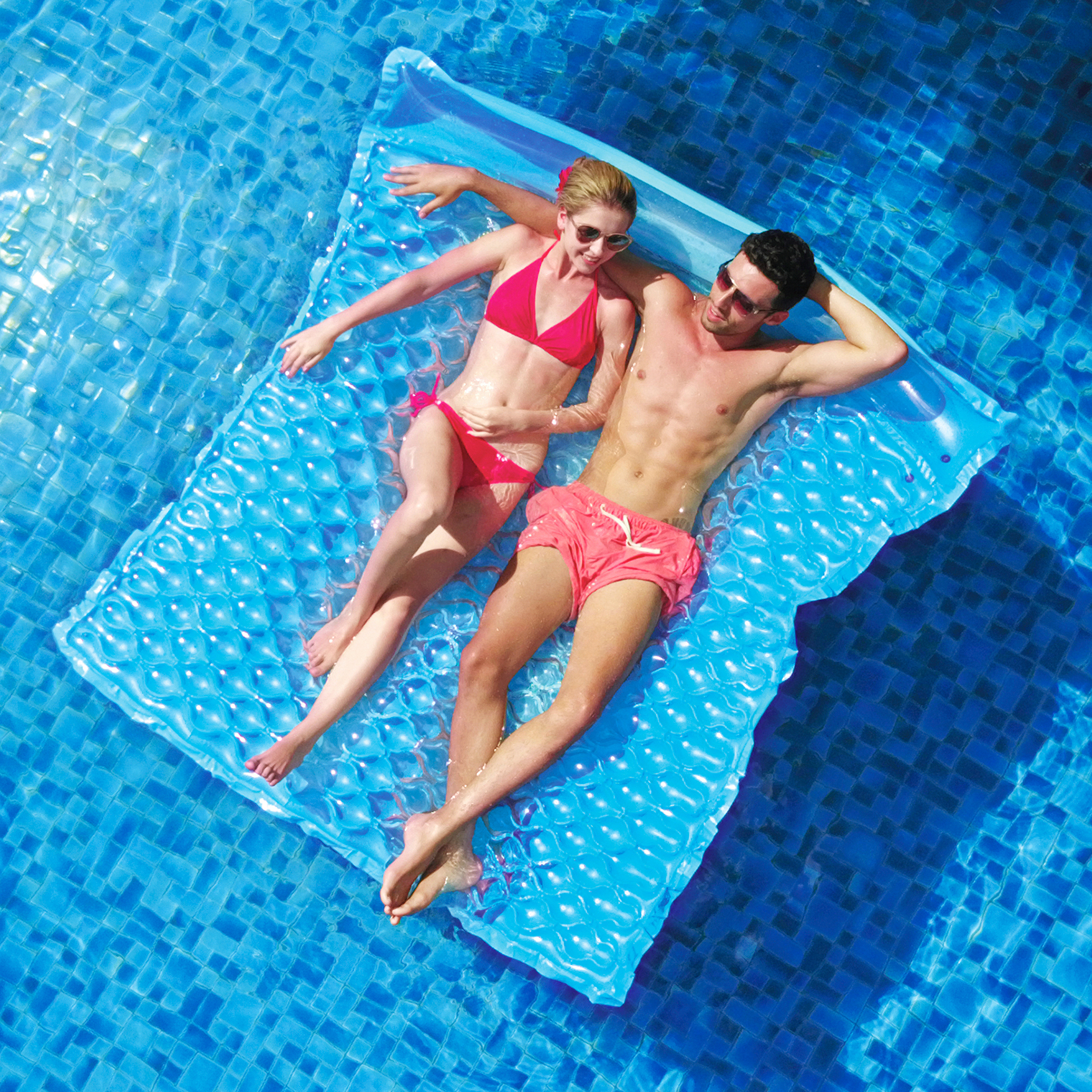 Matelas gonflable bleu Jilong Wave Mat Duo pour 2 personnes, structure gaufrée et appuie-tête, flottant sur une piscine avec deux adultes allongés, idéal pour détente à la piscine, plage ou lac.