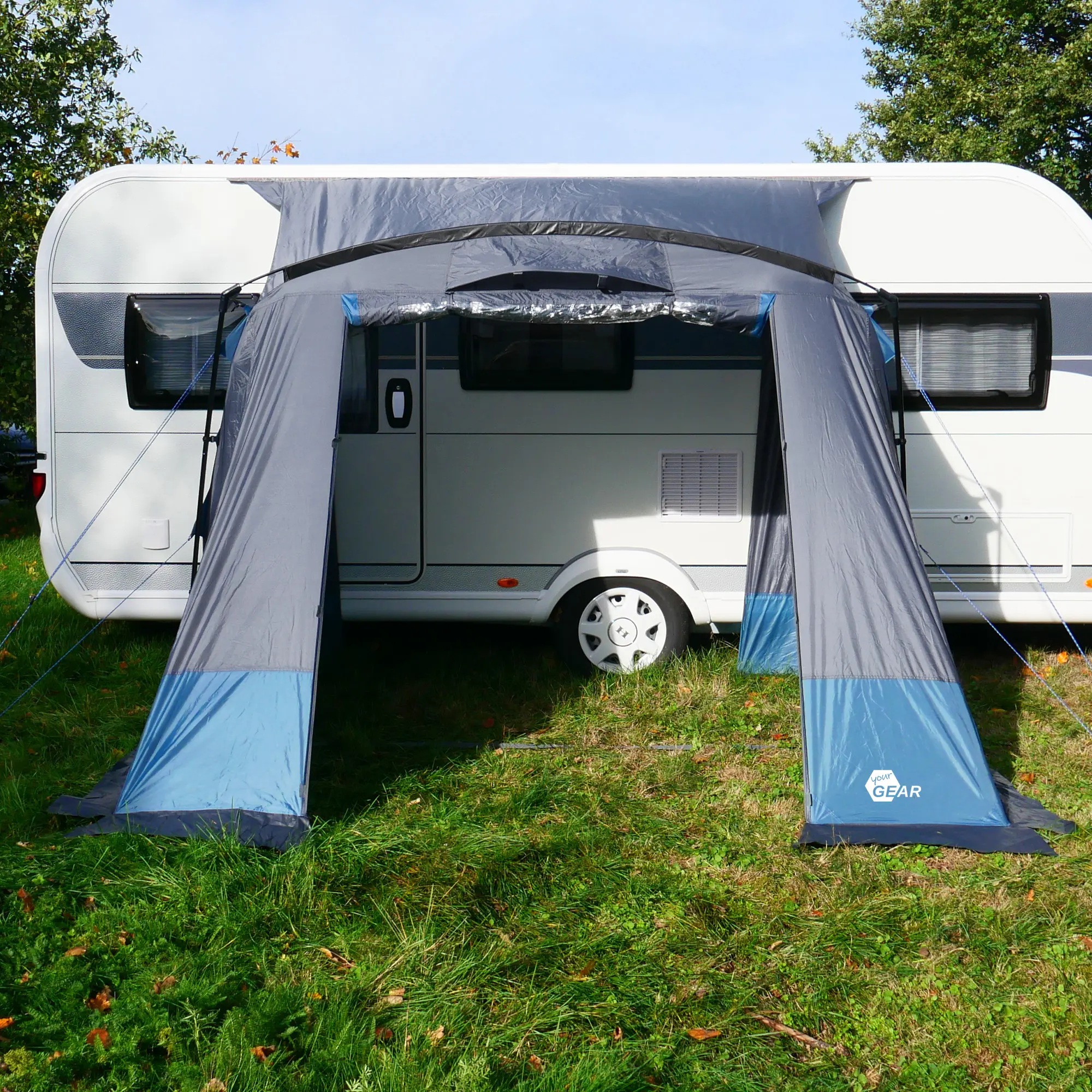 Avance de caravana your GEAR Pampero 280 gris y azul, con dos entradas, gran ventana frontal y material resistente al clima, instalado en un lateral de caravana sobre césped. Ideal para camping y viajes.