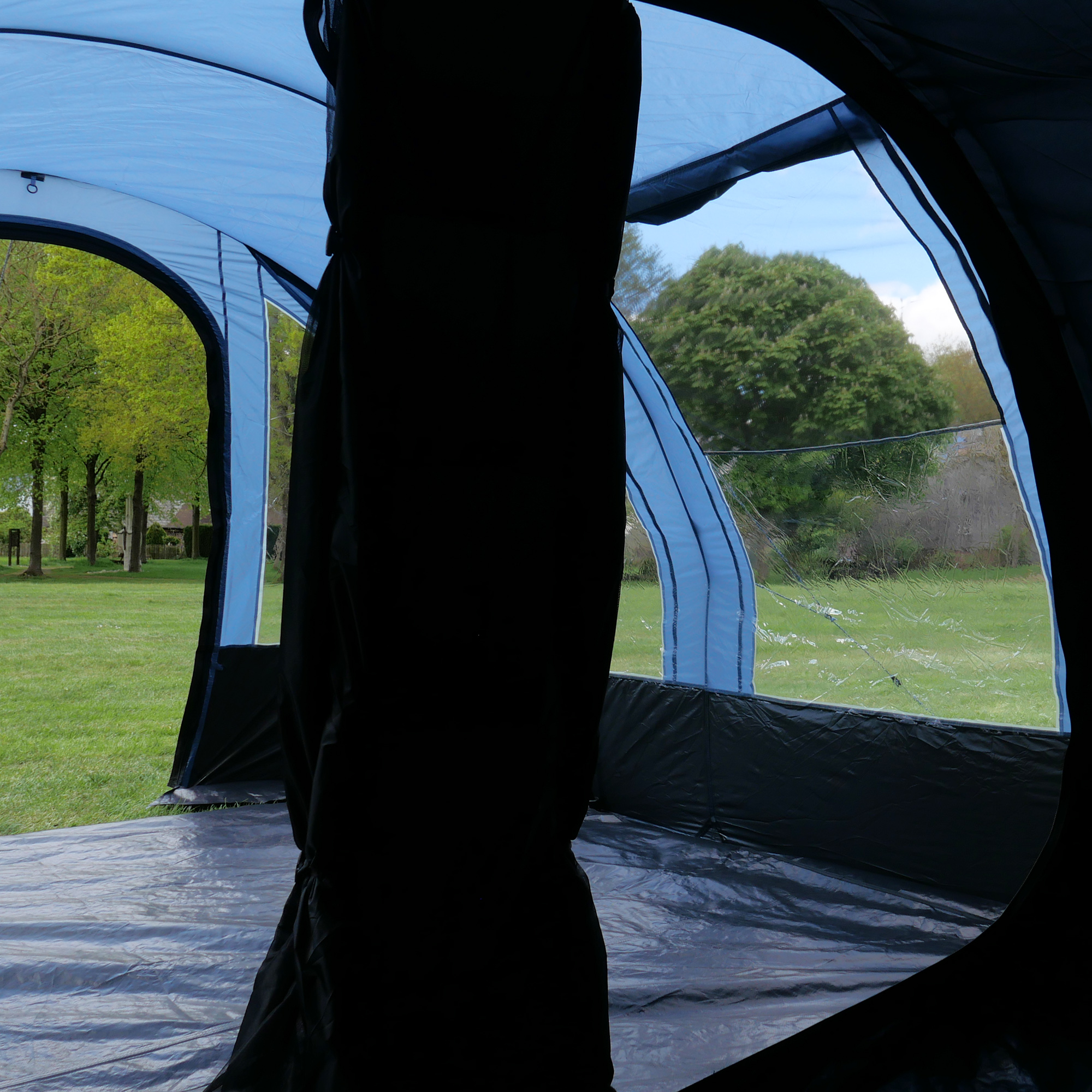Vue intérieure du your GEAR Mistral, tente tunnel familiale 6 personnes, grandes fenêtres transparentes, compartiment de couchage divisible, hauteur permettant de se tenir debout, tissu bleu, sol intégré, vue sur la pelouse.