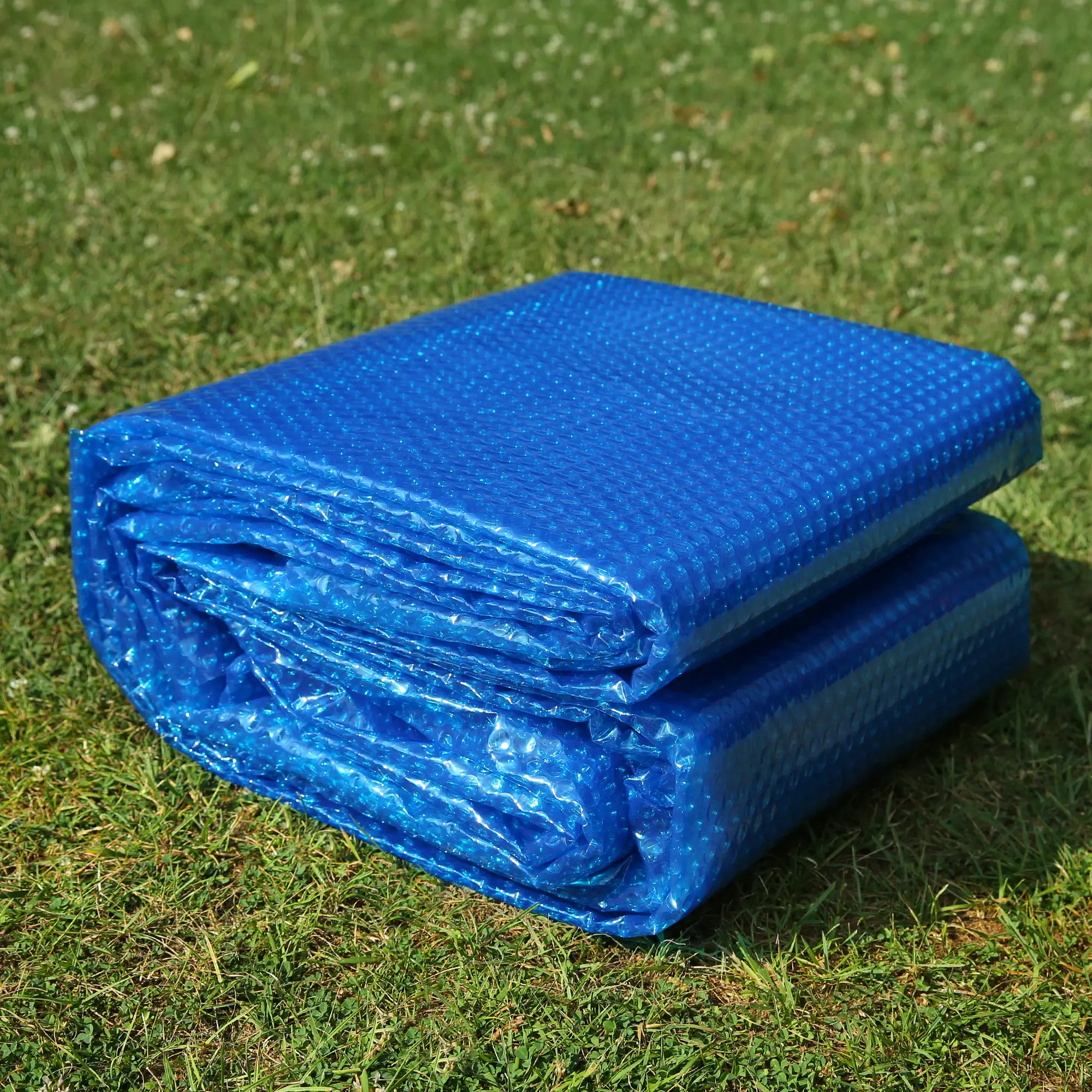 Bâche solaire rectangulaire bleue yourGEAR SC-300x200 pour piscine, épaisseur 300 µm, structure à bulles visible, pliée et posée sur une pelouse, idéale pour chauffer l’eau du bassin avec l’énergie solaire.