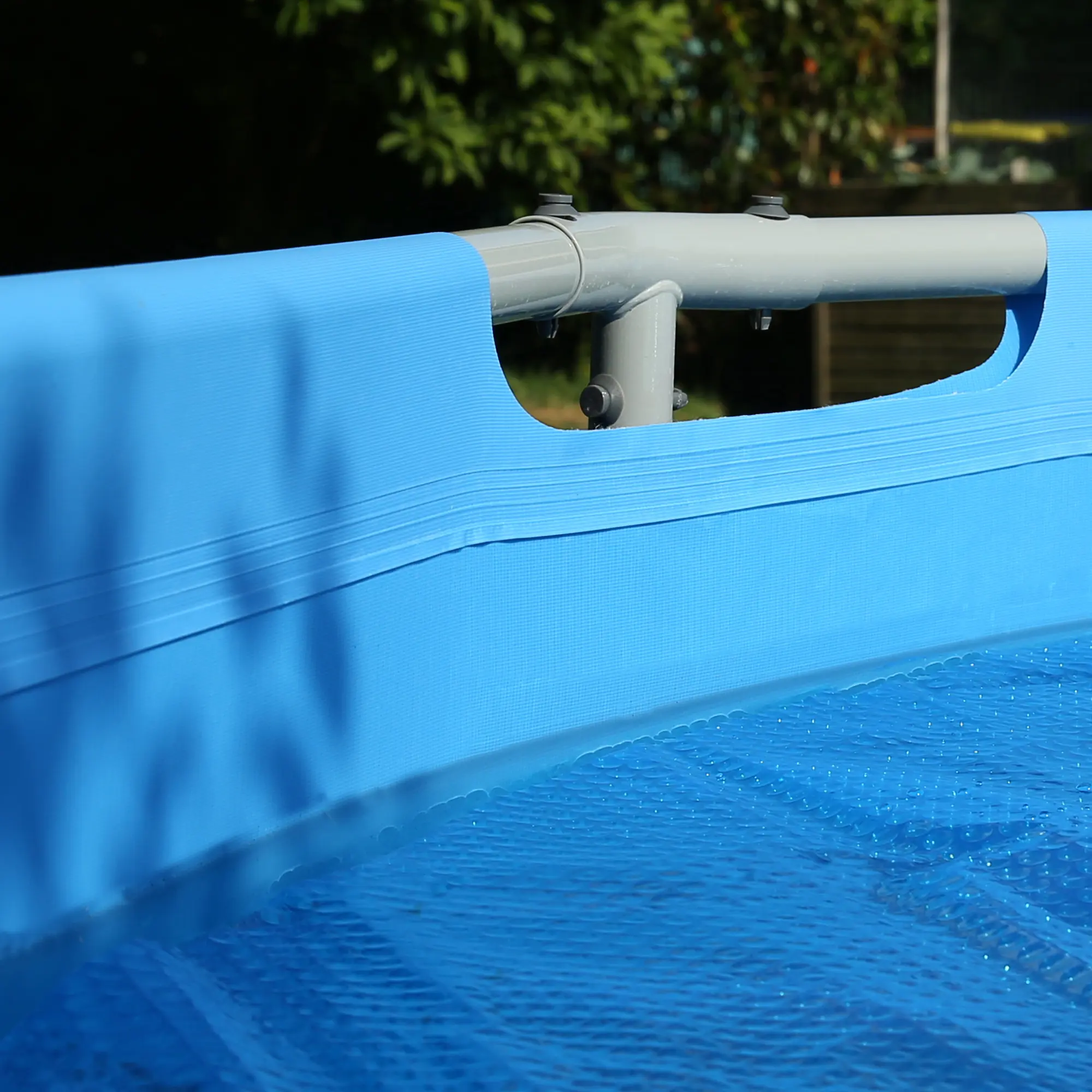 Telo rotondo di una piscina con copertura yourGEAR Solarplane SC-Ø-305; spessa pellicola solare blu a bolle galleggiante sull’acqua, struttura piscina visibile, ideale per riscaldare l’acqua tramite energia solare.