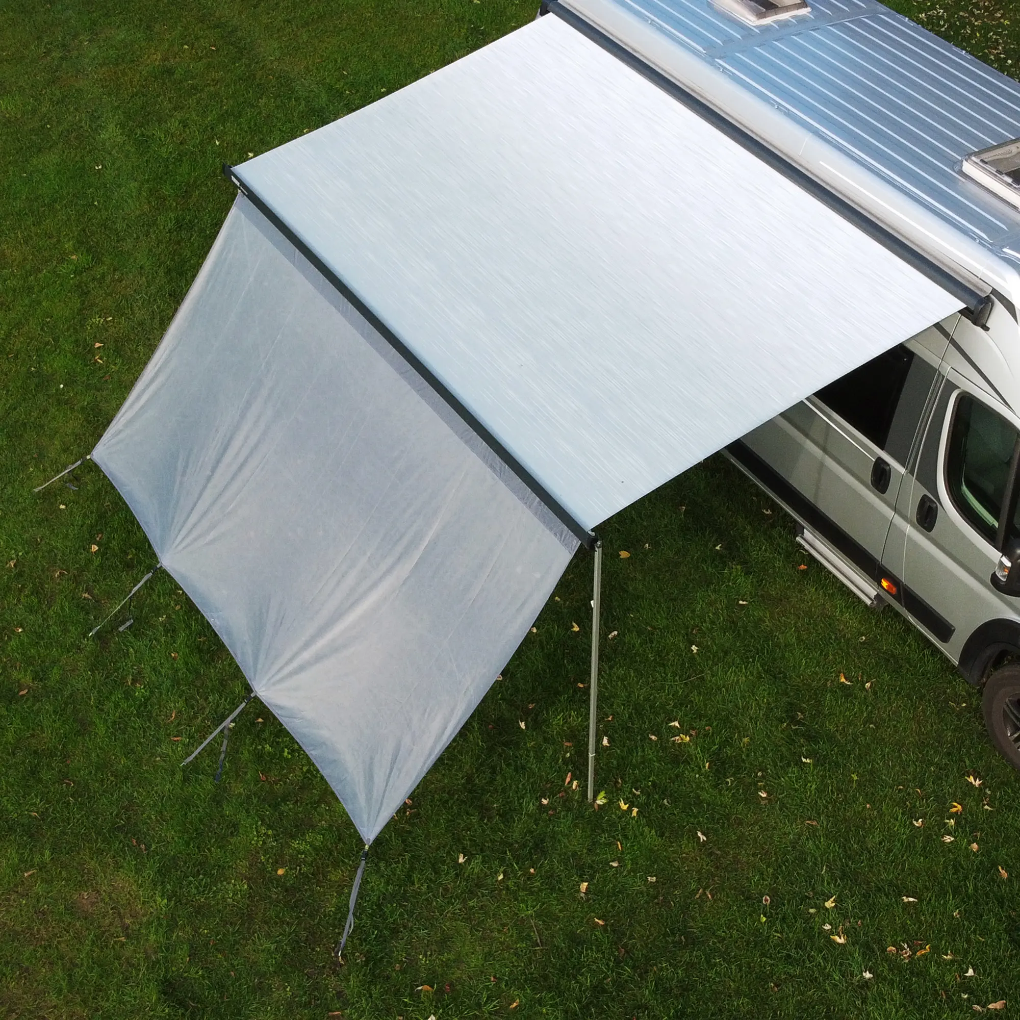 Vorderwand your GEAR Capri Sun Blocker 2,8 x 2 m an Markise eines Wohnmobils, lichtdurchlässiges Gewebe als Sonnen- und Sichtschutz, mit Abspannleinen und Kederleiste, auf grünem Rasen installiert.