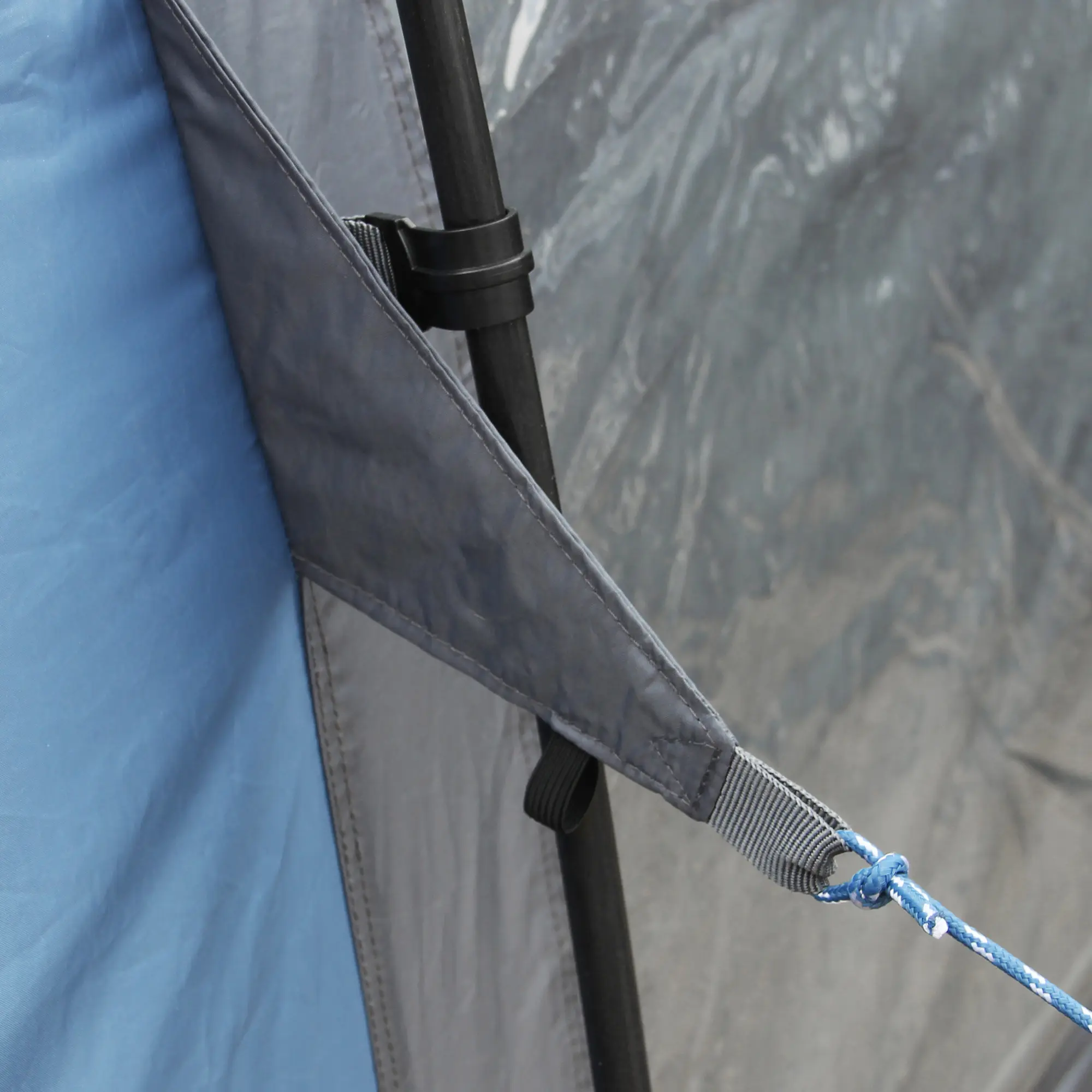 Dettaglio del your GEAR Busvorzelt Rimini 300: angolo della tenda con tessuto blu e grigio, paleria nera e corda di fissaggio blu, che evidenzia la robusta costruzione e materiali resistenti del tunnel autoportante.