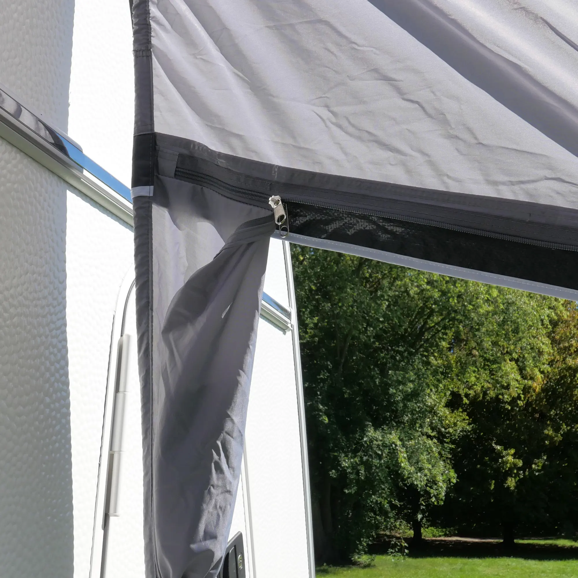 your GEAR Vicenza 350E AIR inflatable awning attached to a caravan, showing the durable grey fabric, zipper system, and single air tube frame with sunlight and green trees in the background.