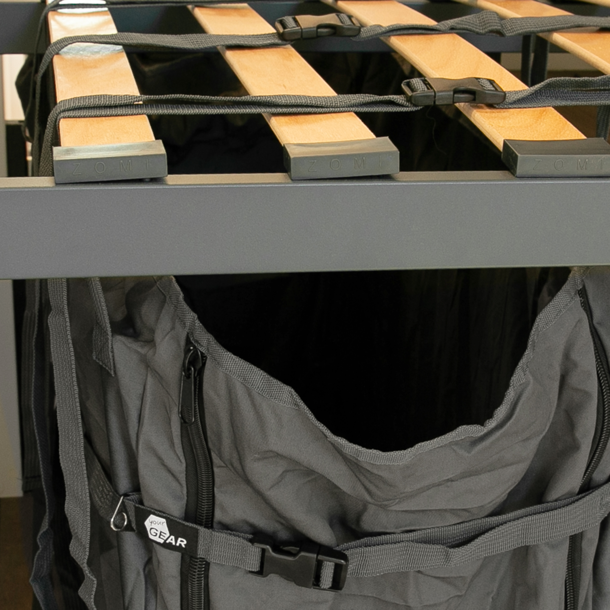 your GEAR Bozen storage bag for camper van rear garage, shown vertically mounted under a slatted bed frame, made of durable black fabric with zipper and buckle, ideal for organizing camping furniture and accessories.
