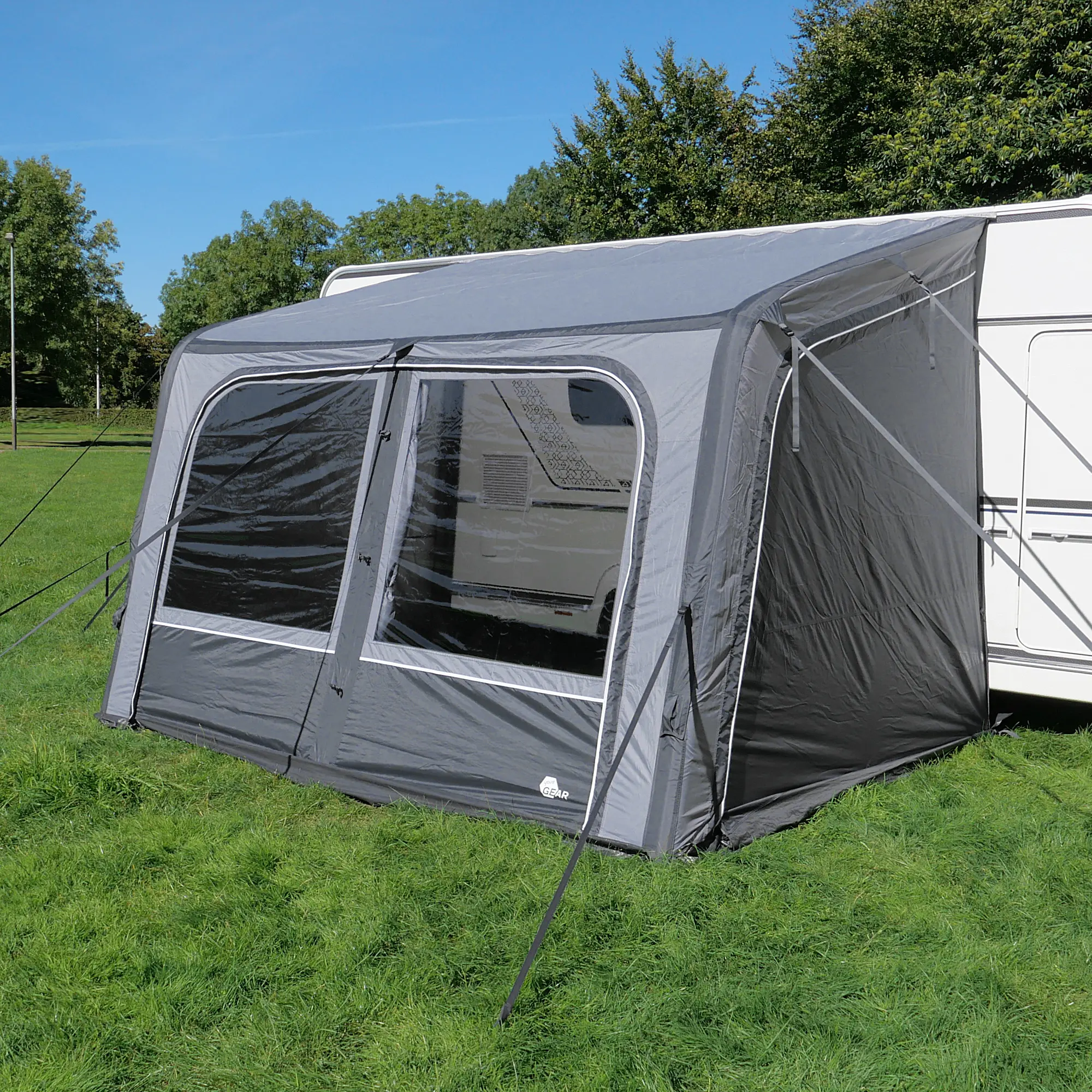 Avance de tu caravana con el your GEAR Porto 340 Air, un toldo inflable gris oscuro con ventanas grandes, estructura de aire y fácil montaje, conectado a un vehículo sobre césped verde bajo cielo azul.