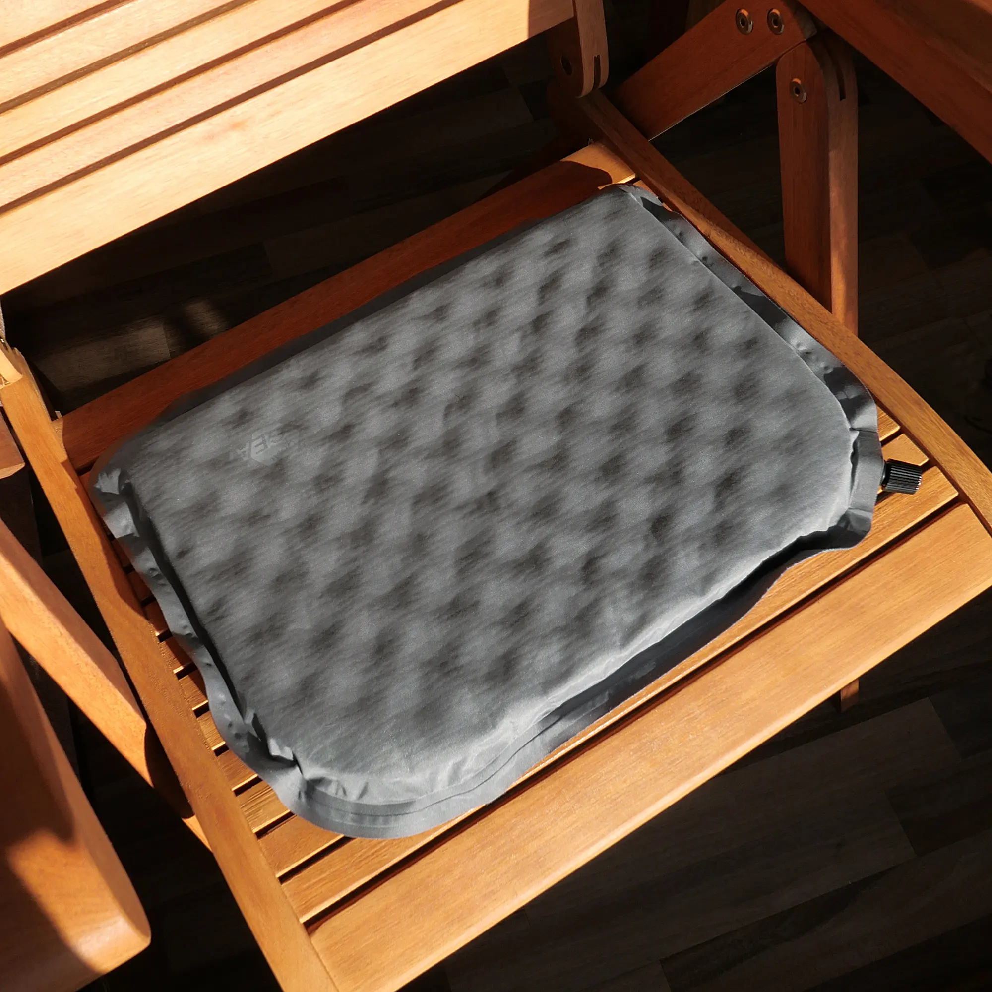 Self-inflating yourGEAR thermal seat cushion, grey, 40x30x3.5cm, with foam core, shown placed on a wooden chair. Ideal for camping, travel, and outdoor seating comfort and insulation.