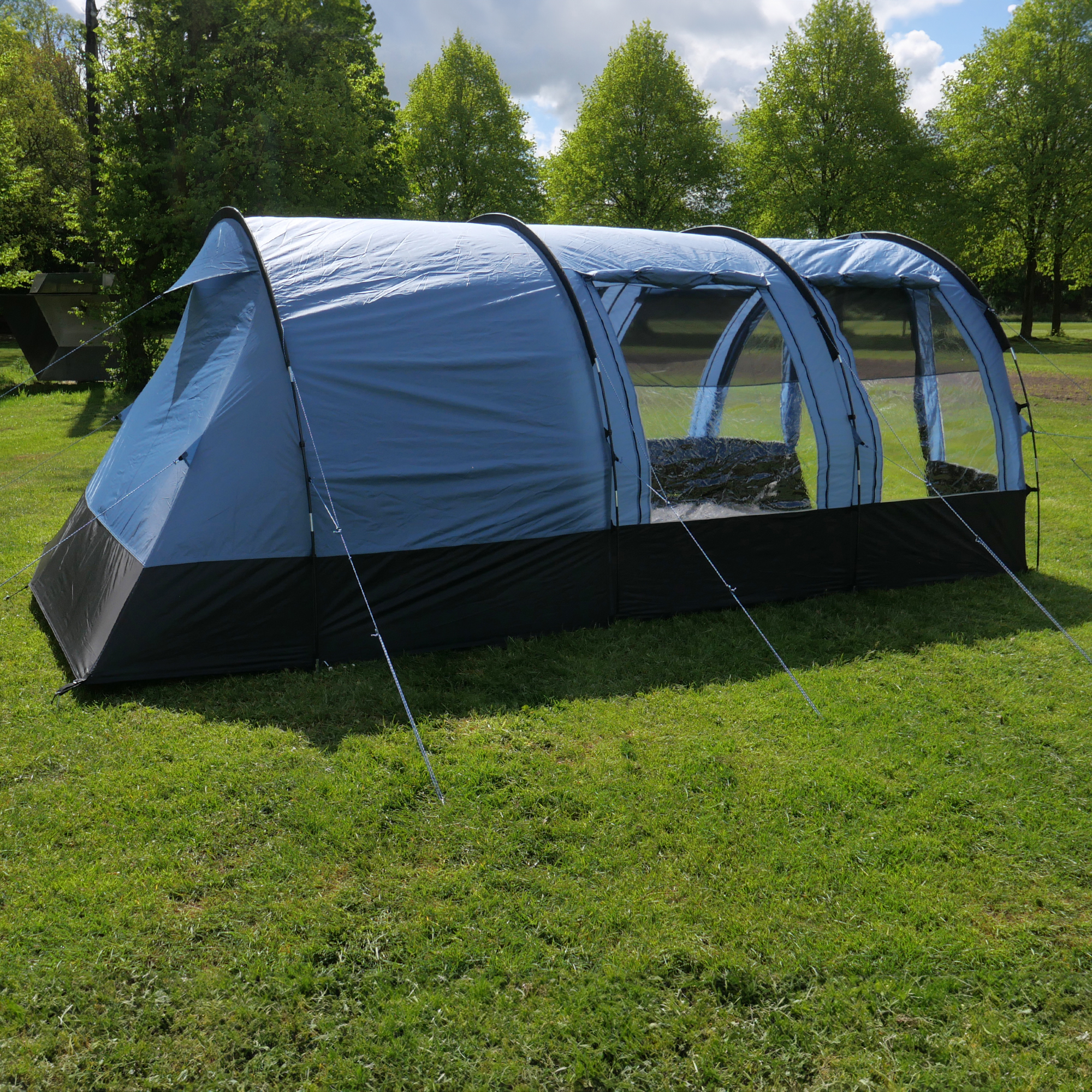 Tente tunnel familiale your GEAR Mistral pour 6 personnes, 490 x 325 x 195 cm, grande surface habitable, fenêtres transparentes latérales, tissu bleu avec base noire, installée sur pelouse verte.
