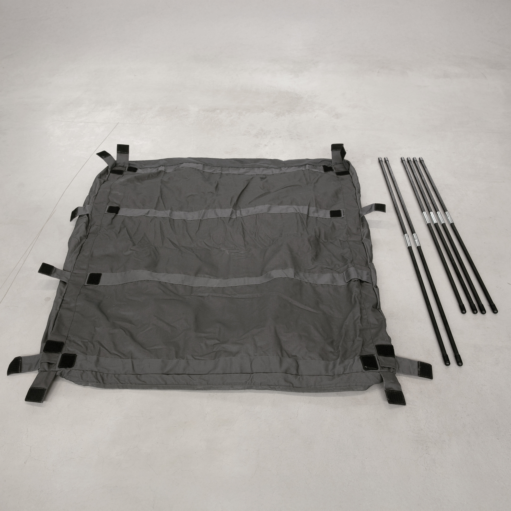 Bolsa de almacenamiento your GEAR Catania para camper, en color gris, extendida en el suelo con correas laterales y tubos metálicos desmontables a un lado, ideal para organizar la zona de carga en caravanas.