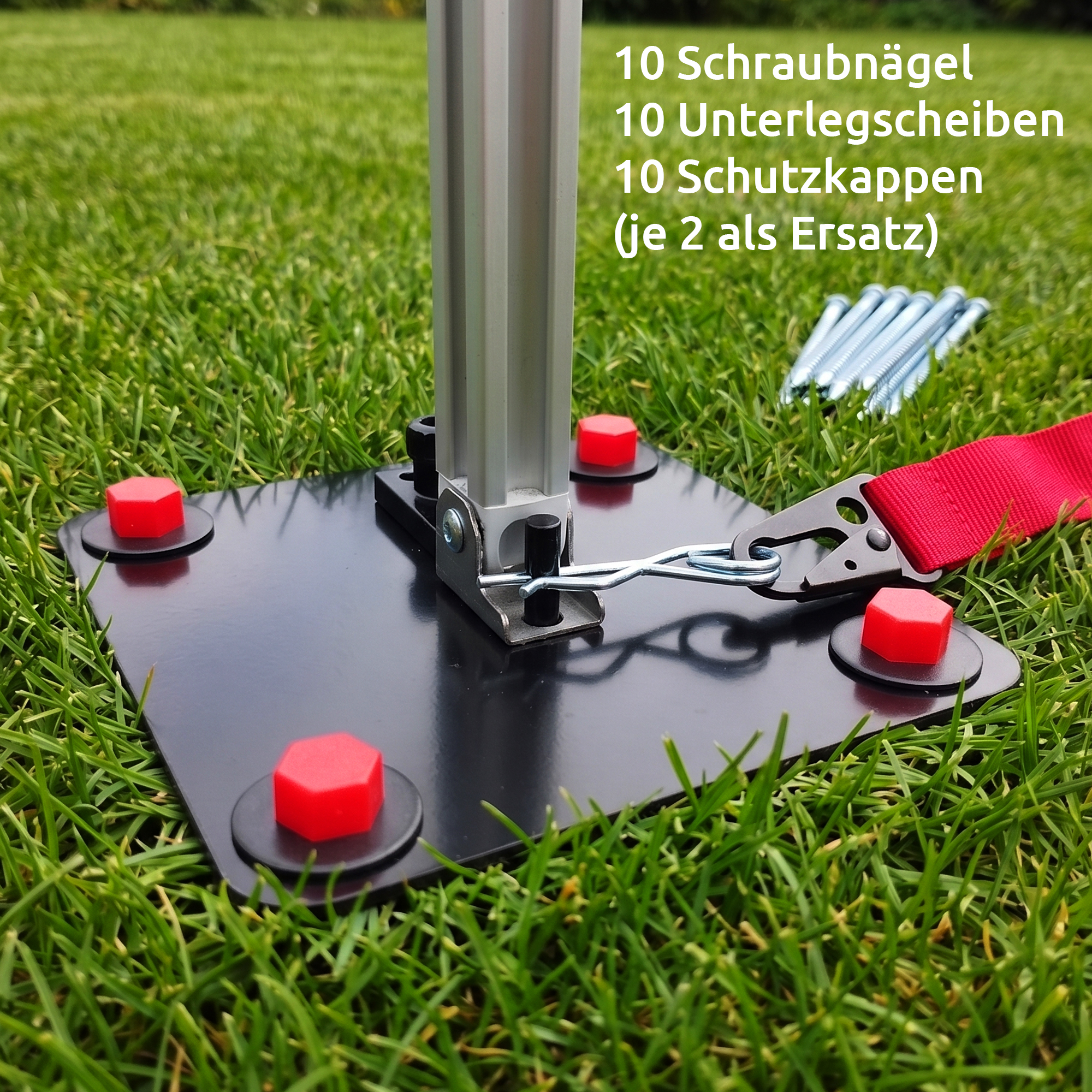 Black metal anchor plate with vertical aluminum awning foot, red plastic caps on four mounting points, retaining clip and red strap laid on grass — your GEAR Montana awning ground anchor set.