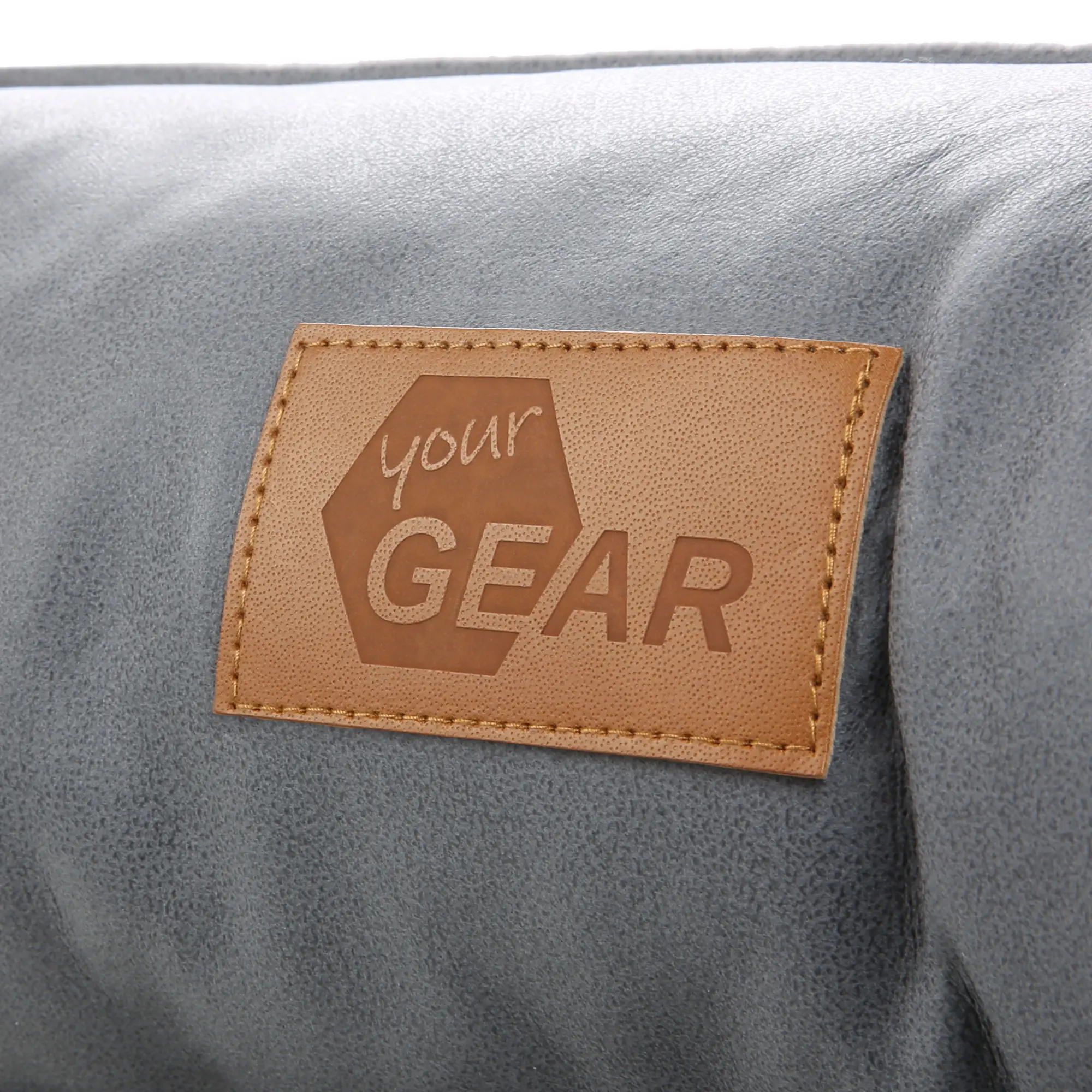 Primer plano de la etiqueta de cuero cosida con el logotipo "your GEAR" sobre la superficie gris del cómodo y lavable colchón para perros Belluno de 60 x 80 cm, certificado OEKO-TEX.