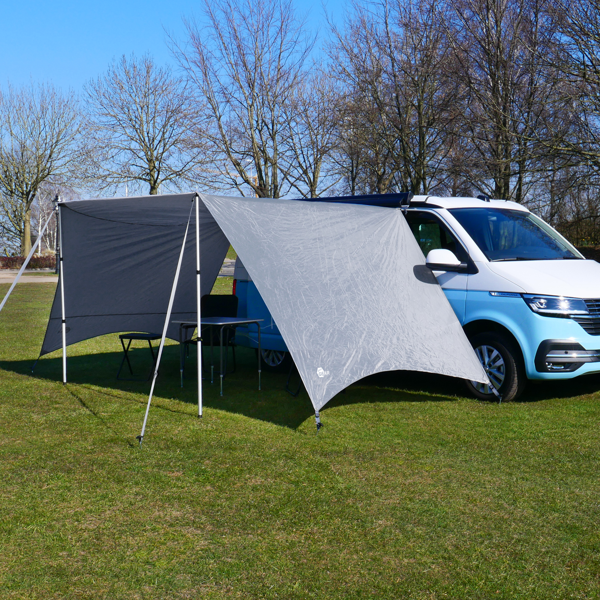 Toldo your GEAR Tropea para furgoneta o camper, color gris, con protección UV 50+, dos paredes laterales y postes de aluminio. Instalado como avance, ofrece sombra y protección junto a una furgoneta blanca.