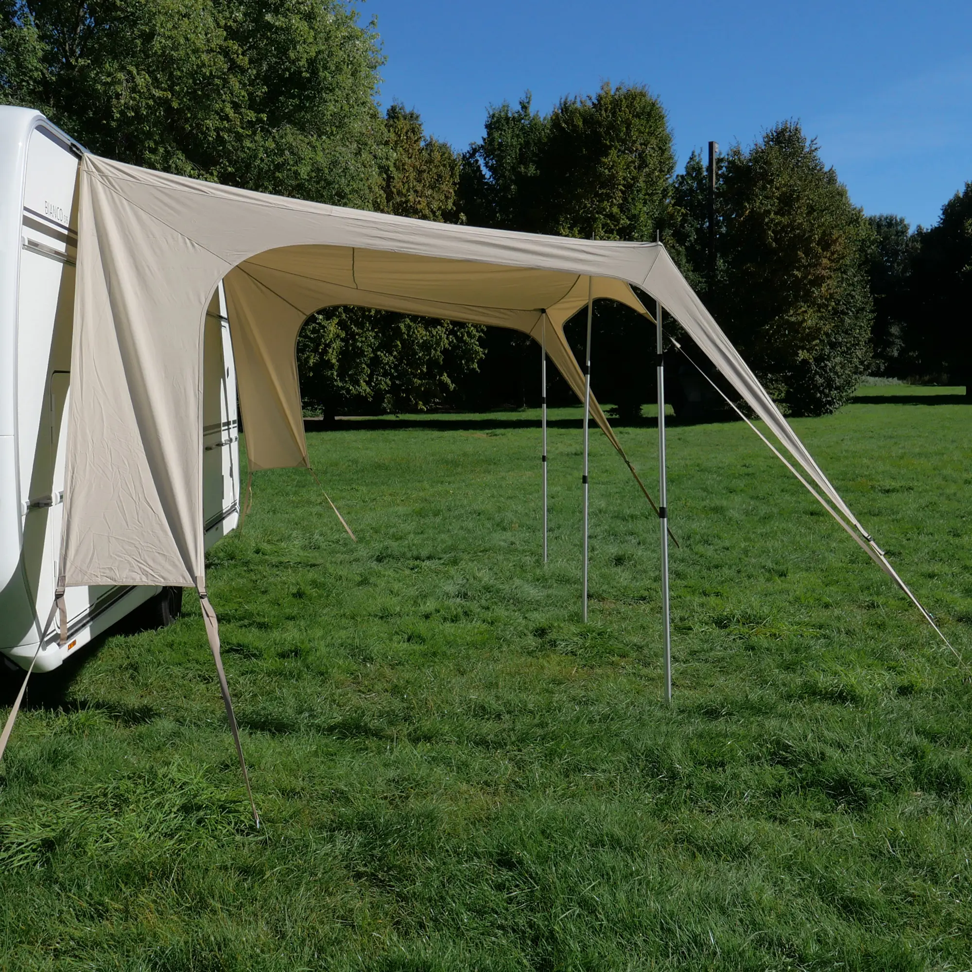 Beiges your GEAR Scilla TC Caravan Tarp Sonnensegel, 400x250 cm, am Wohnwagen montiert. Robustes, atmungsaktives Material mit hohem Baumwollanteil. Schützt vor Sonne und UV, stabil mit Stangen aufgestellt.