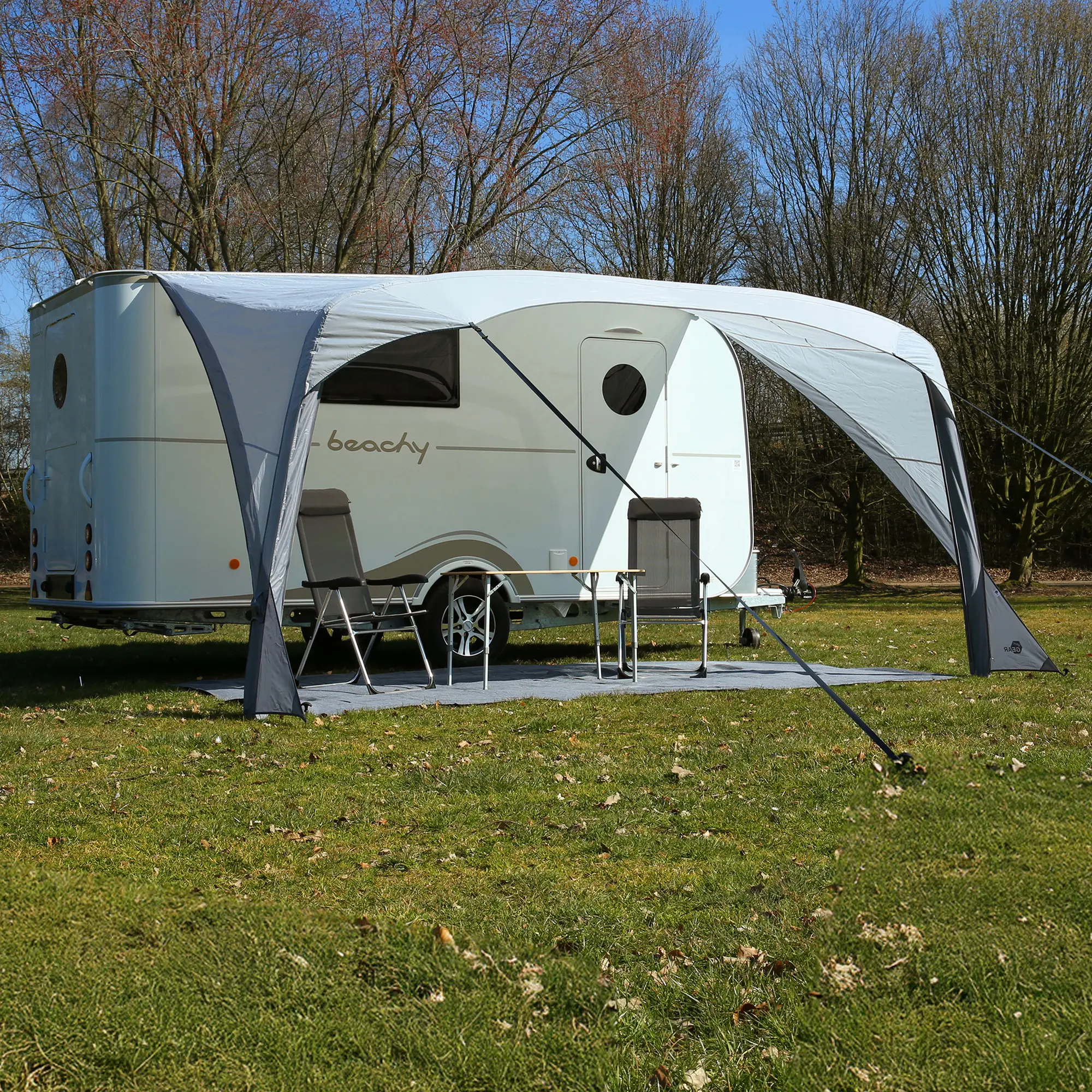 your GEAR Amalfi Air 360 inflatable sun canopy attached to a Hobby Beachy caravan, providing tailored shade and weather protection; includes camping chairs and table set up underneath on grass.