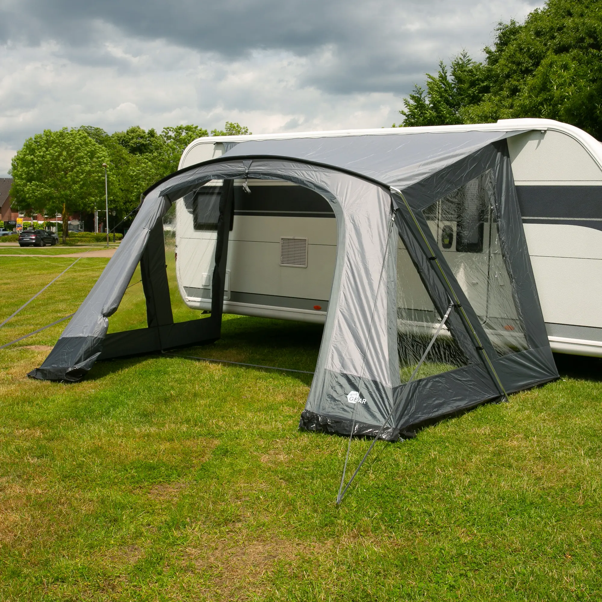 Avance de caravana your GEAR Positano 330 gris con 4 ventanas grandes y puerta amplia, tejido Oxford resistente, estructura de aluminio y protección UV 50+, montado junto a una caravana sobre césped.