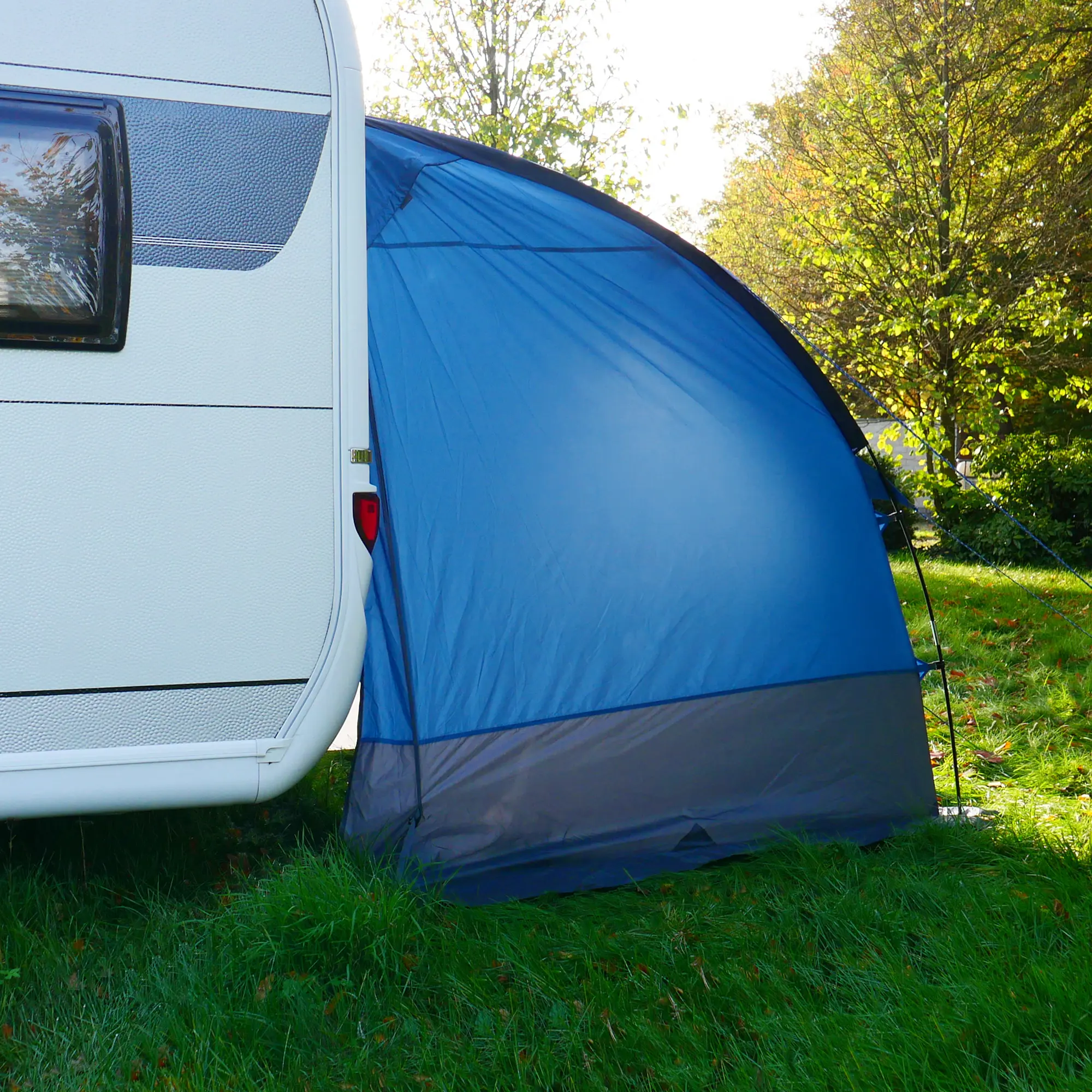 Carpa trasera your GEAR Venecia azul y gris, acoplada al extremo de una caravana, ideal como toldo, almacén o cocina, con entrada amplia y suelo incluido, sobre césped en entorno natural.