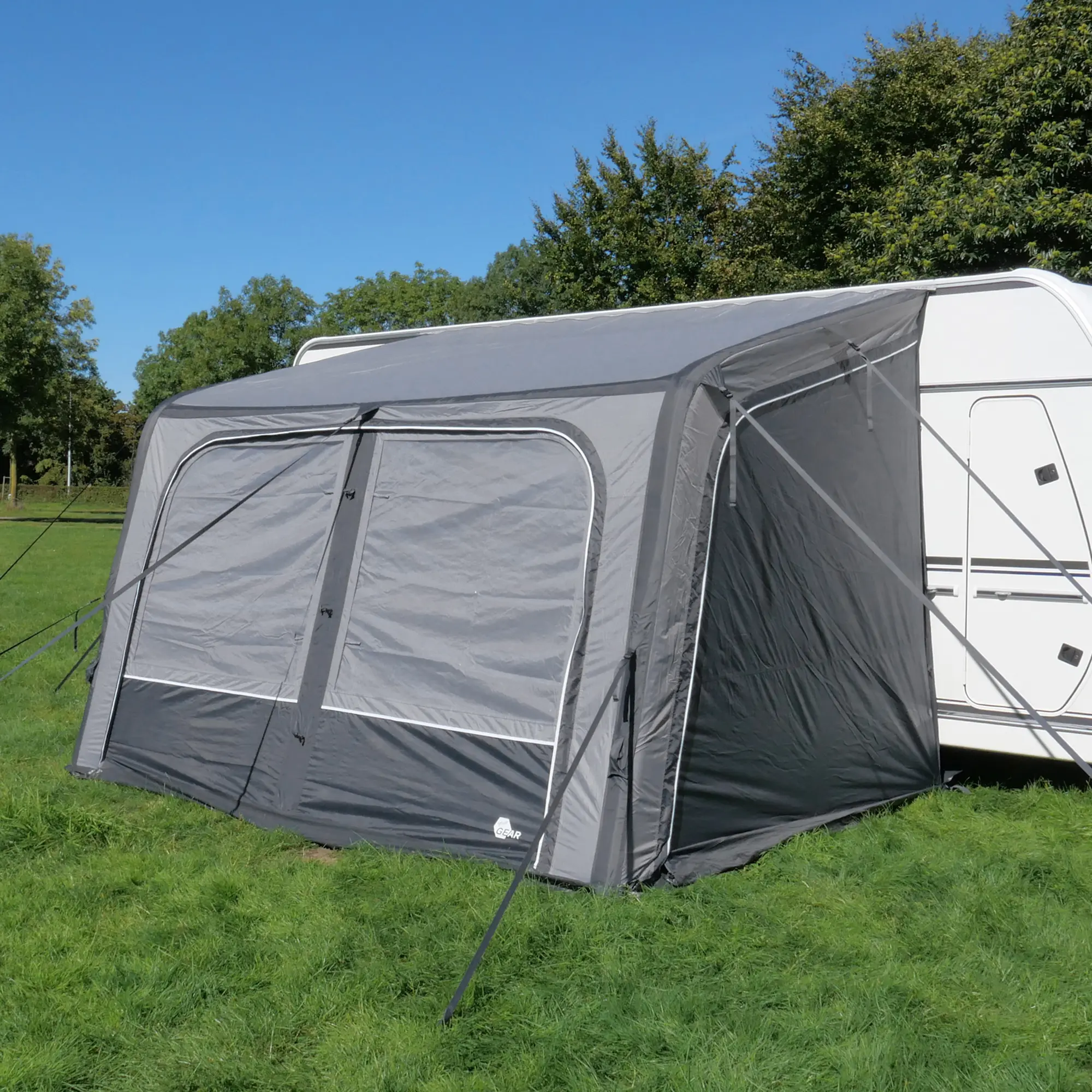 Vorzelt your GEAR Porto 340 Air in Grau, aufblasbar, mit großen Fenstern, an einem weißen Wohnwagen angebracht, steht auf grüner Wiese, ideal als Sonnenvordach und Wetterschutz für Caravan und Wohnmobil.