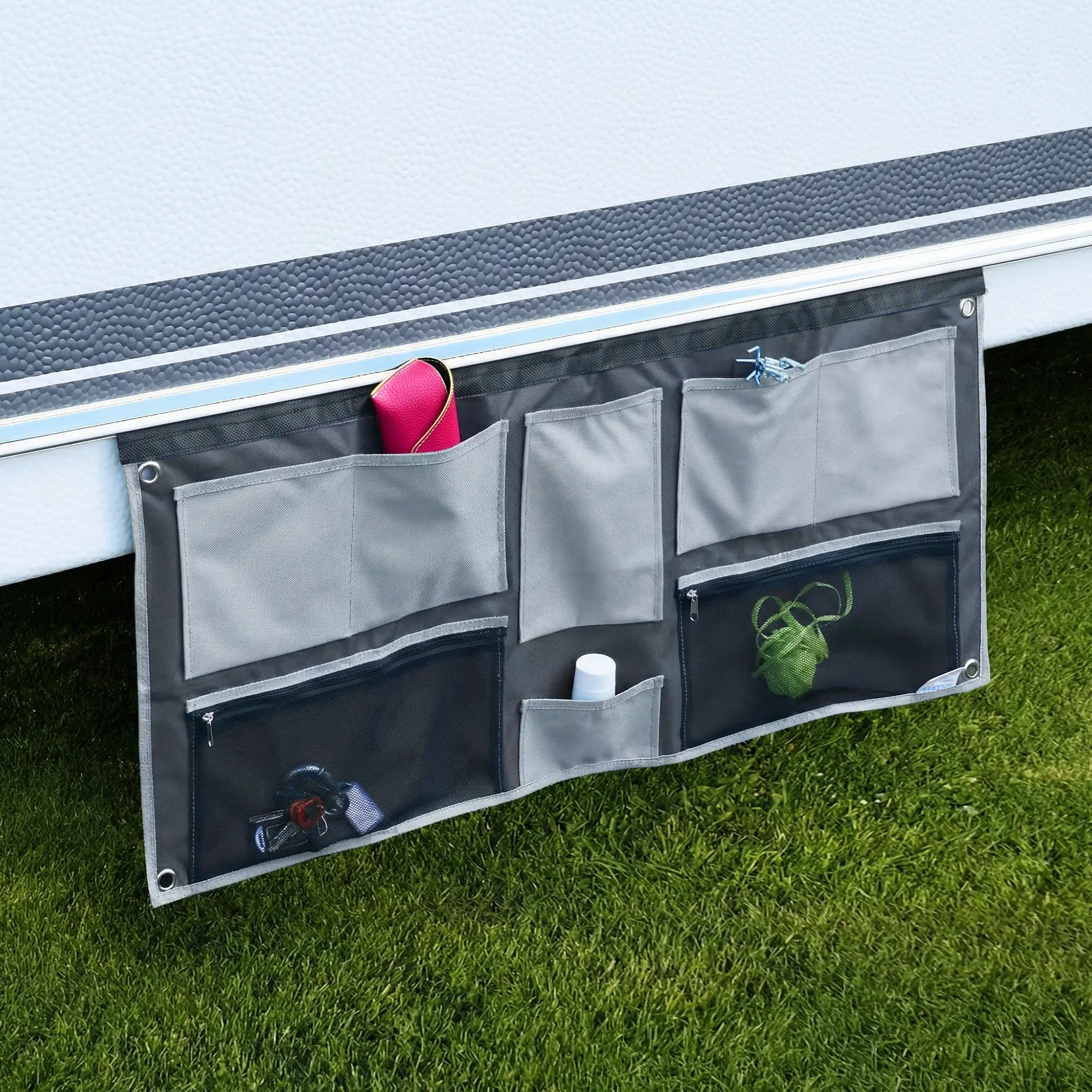 Organiseur de caravane gris your GEAR suspendu par keder, avec plusieurs poches ouvertes et zippées en tissu et mesh, œillets métalliques aux coins, rangement pour clés, bouteille et petits objets, fixé sous la paroi du camping-car.
