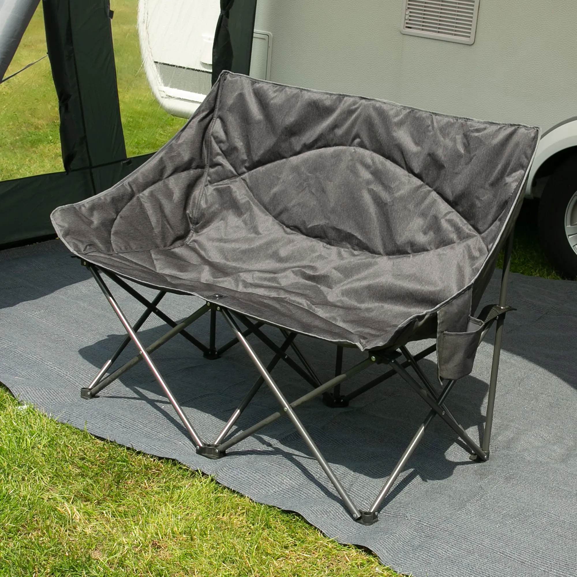 XXL Campingsofa your GEAR Modena für 2 Personen, gepolstert, extra breite Sitzfläche, stabile Stahlkonstruktion, in Two-Tone-Optik, faltbar, Outdoor geeignet, steht auf Campingmatte vor Wohnwagen.