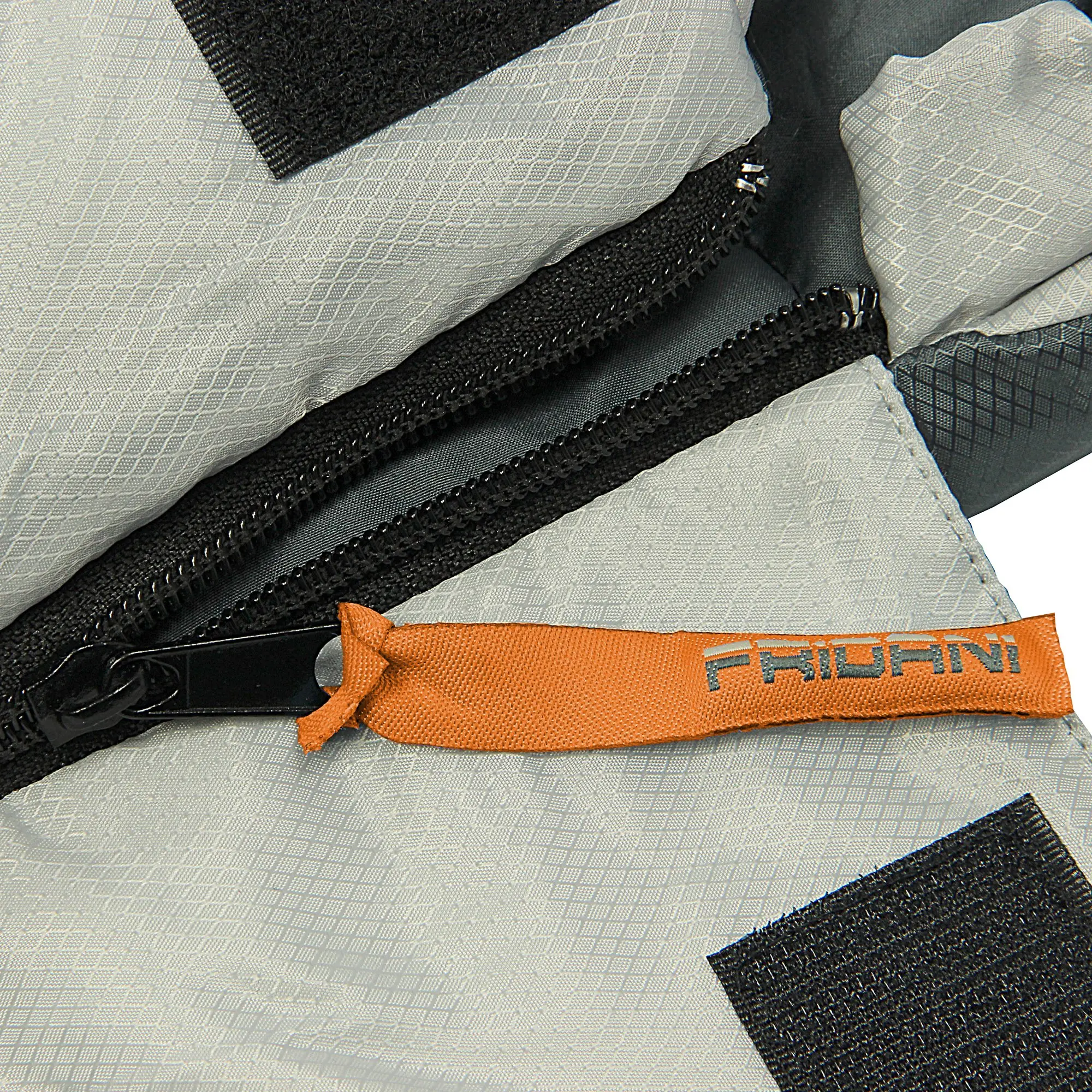 Dettaglio di una cerniera nera su tessuto tecnico grigio con una linguetta arancione con la scritta "PRIOANI" e inserti in velcro nero.