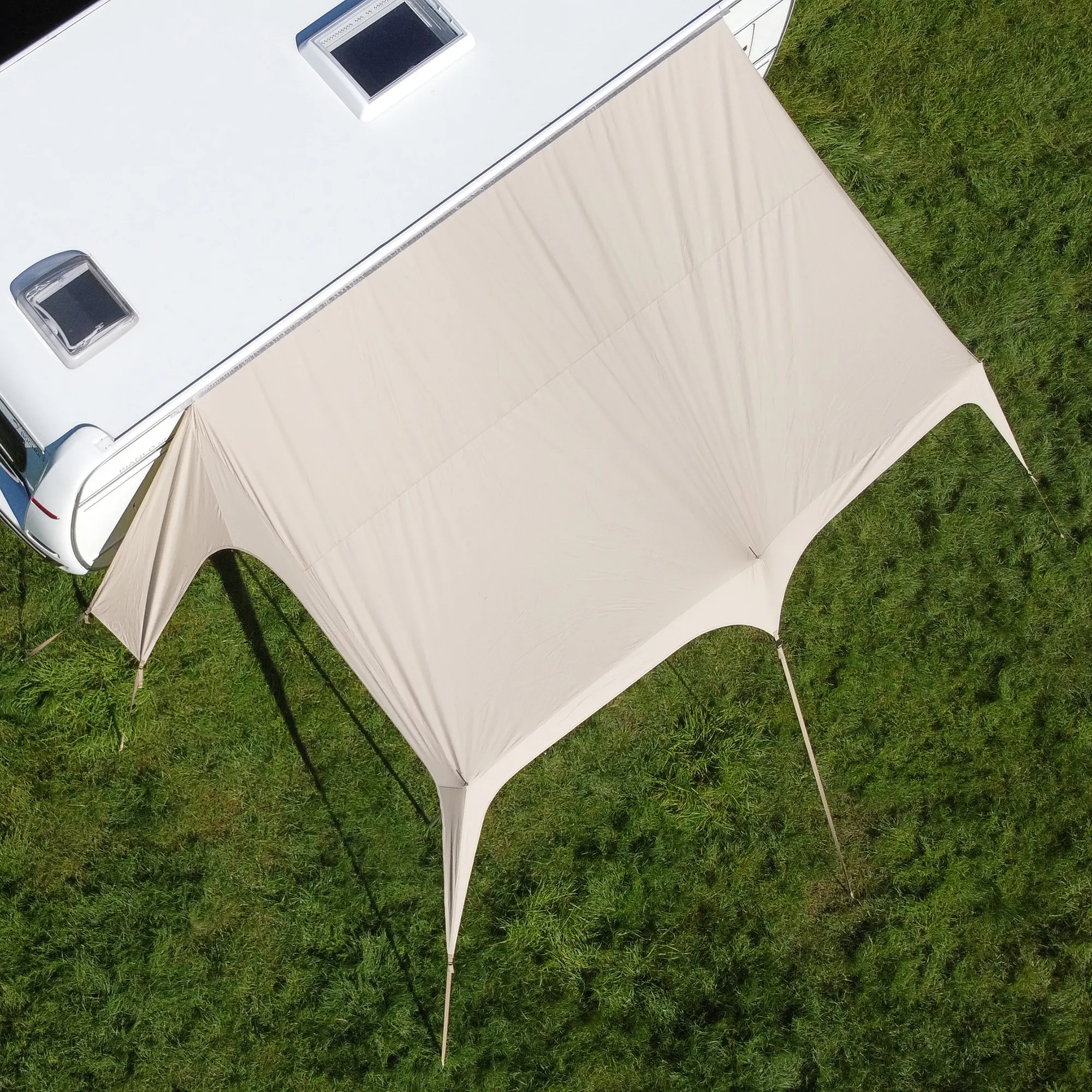 Beiges your GEAR Scilla TC Caravan Tarp Sonnensegel, 400x250 cm, aus atmungsaktivem Baumwoll-Mix, am Wohnwagen montiert, bietet großflächigen Sonnen- und Wetterschutz auf einer grünen Wiese.