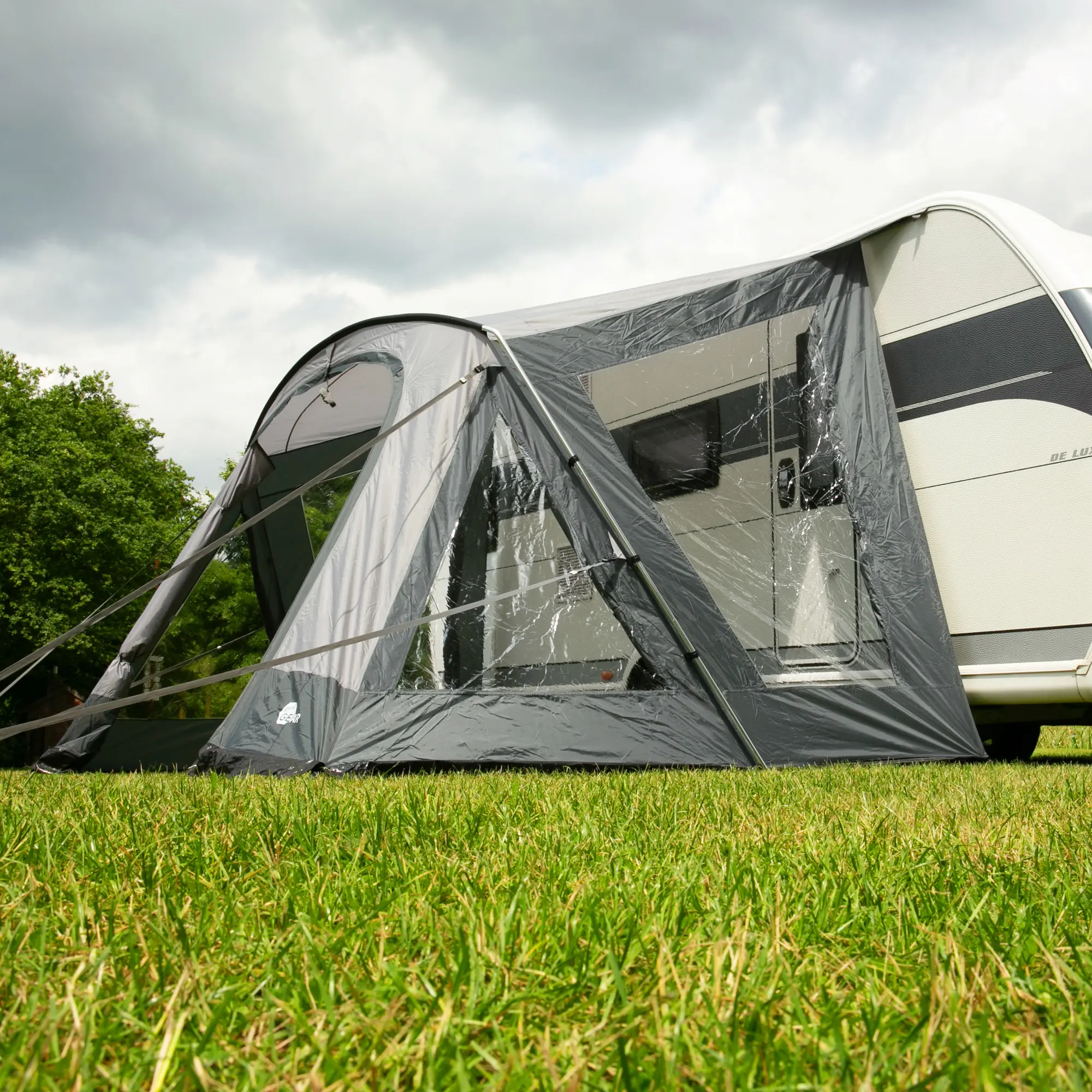 Wohnwagenvorzelt your GEAR Positano 400 mit 4 großen Fenstern, breiter Tür, Sonnendach, robustem Aluminium-Gestänge und UV-Schutz 50+ am Caravan aufgebaut, auf grünem Rasen stehend.