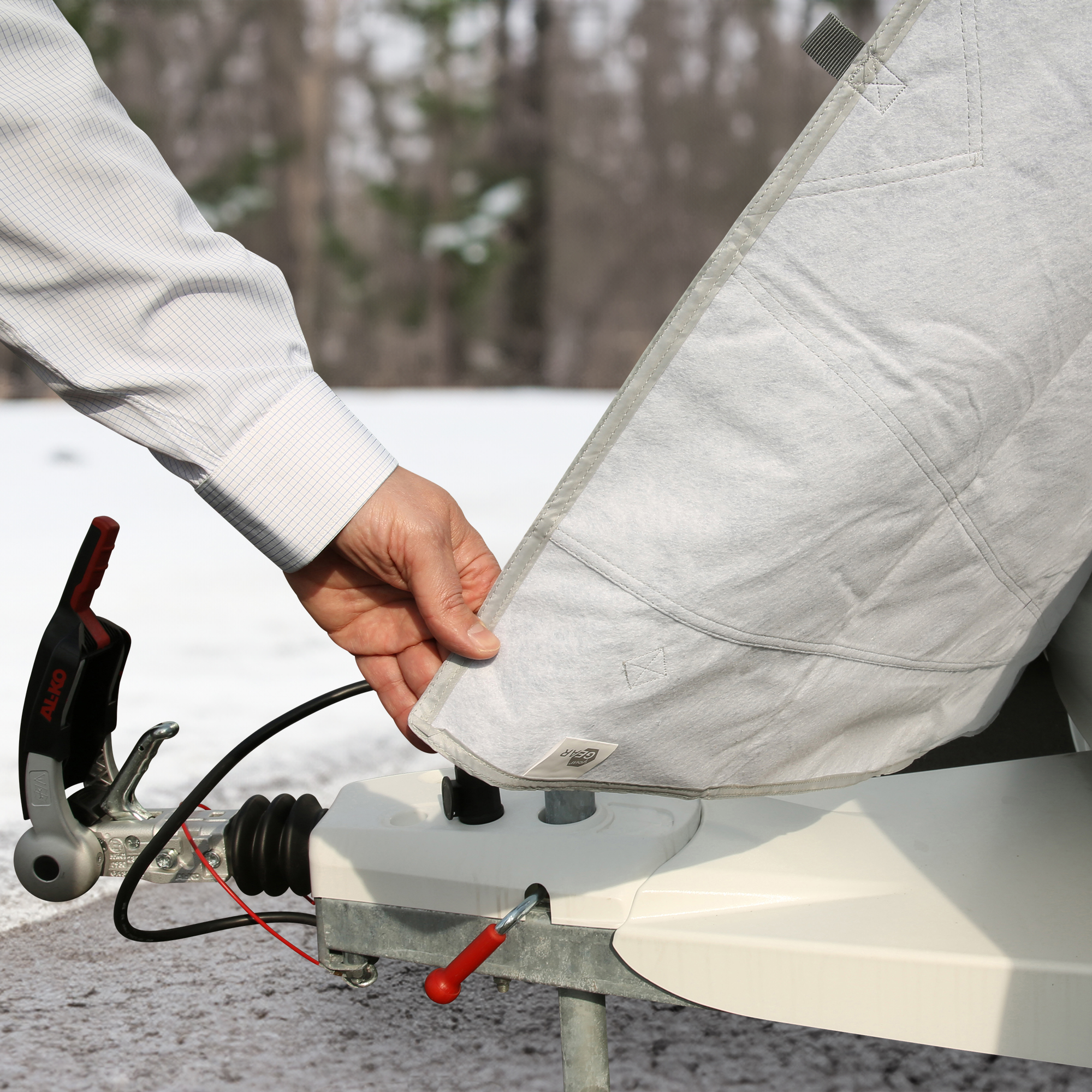 Man attaching your GEAR Caravan Thermo Bug Protection Cover, 200 x 160 cm, to a caravan front in a snowy outdoor setting; grey protective cover designed for winter and summer use.