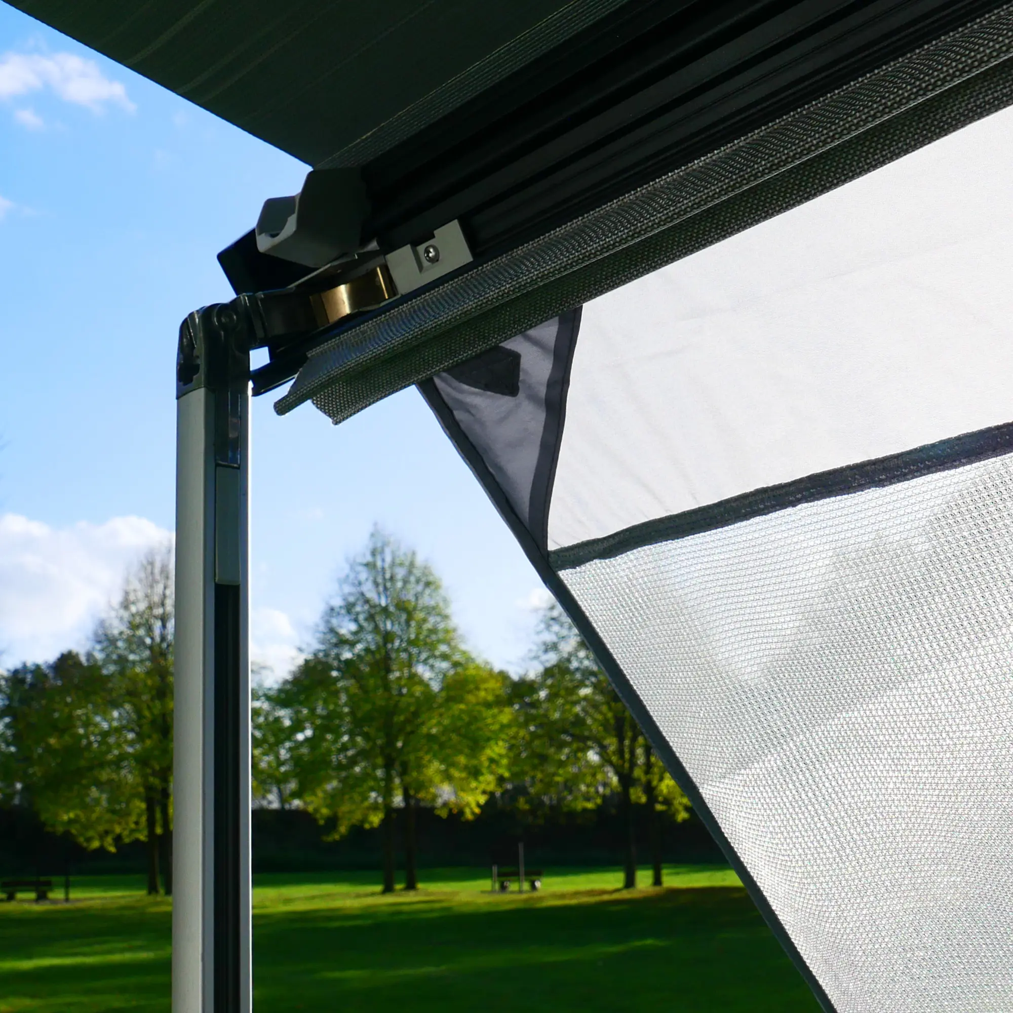 Front view of the your GEAR Capri Sun Blocker 2.4 x 2 m, mounted on a camper awning, showing the light grey mesh fabric for sun and heat protection, with a green outdoor background.