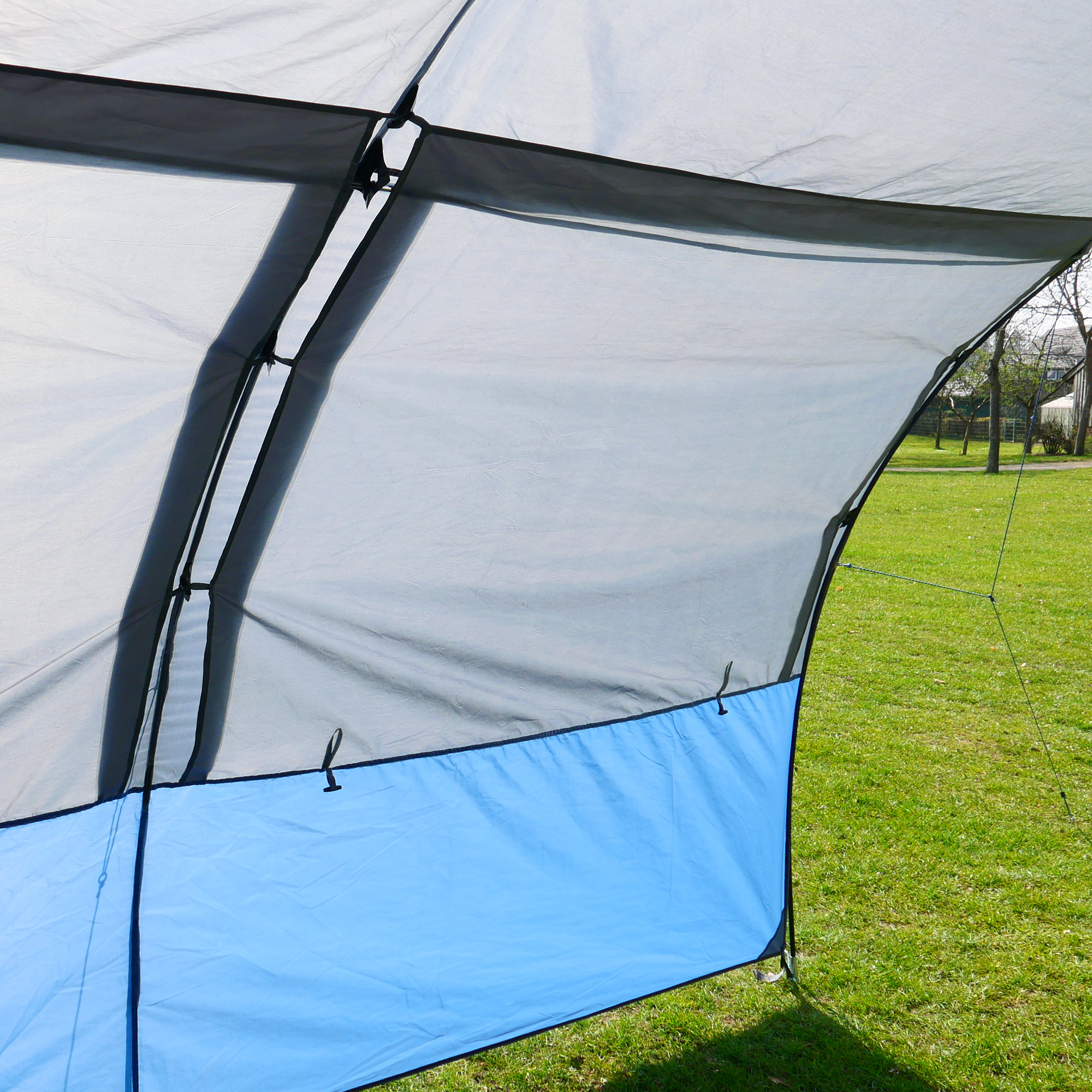Auvent your GEAR Riviera 350 pour caravane ou camping-car, 3,5x2,6m, tissu gris avec panneau inférieur bleu, grande fenêtre panoramique, protection UV 50+, structure légère, installé sur pelouse.