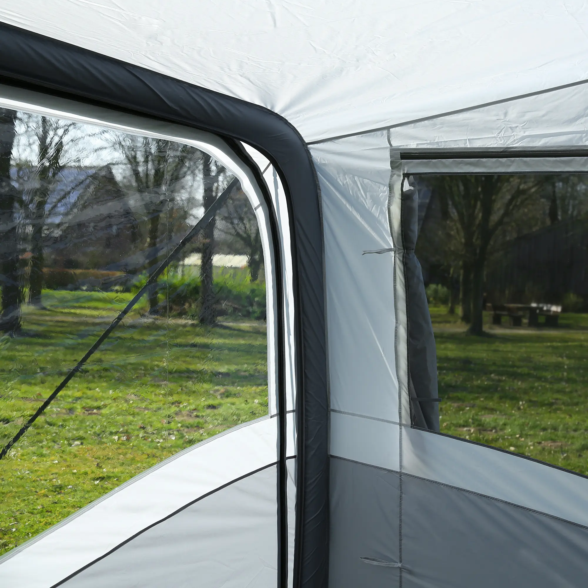 Vue de l’intérieur d’une tente avec fenêtres transparentes donnant sur un jardin verdoyant et des arbres.