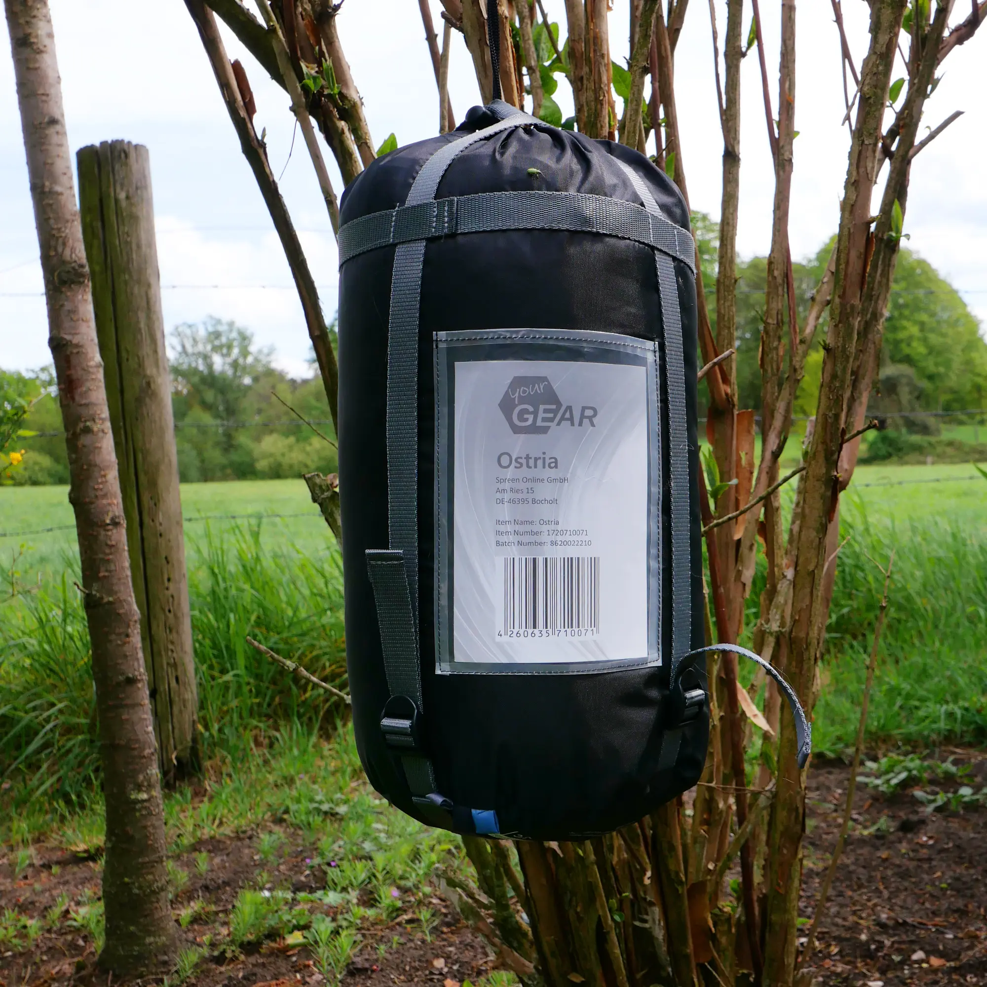 Saco de dormir yourGEAR Ostria azul y gris en bolsa de compresión, tamaño compacto, etiqueta visible, colgado en ramas al aire libre, ideal para verano y trekking, modelo 230x75cm, peso ligero.