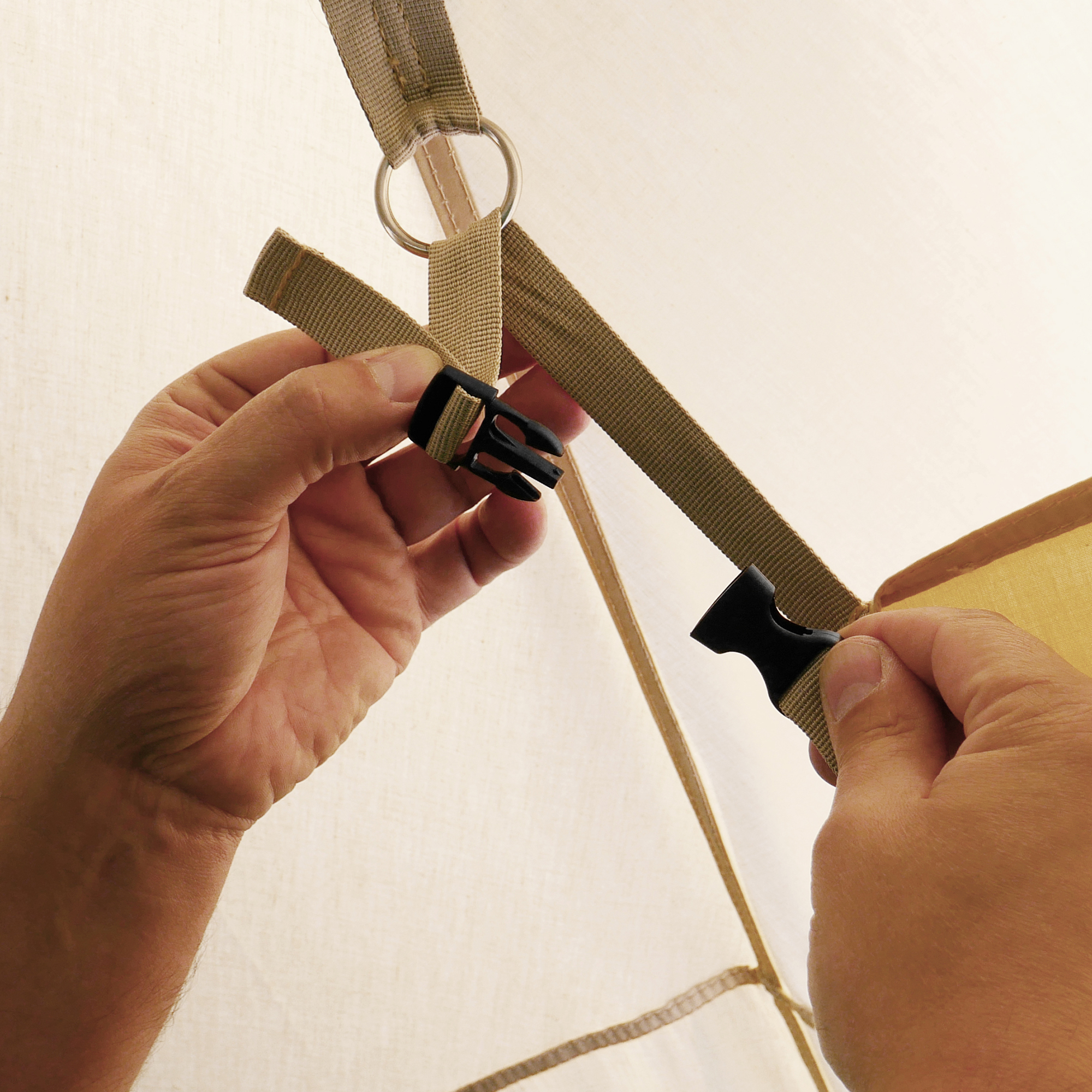 Close-up of hands attaching the your GEAR Sonora Sidewall to a pavilion using sturdy beige straps and a black clip fastener, highlighting the secure and practical installation system.