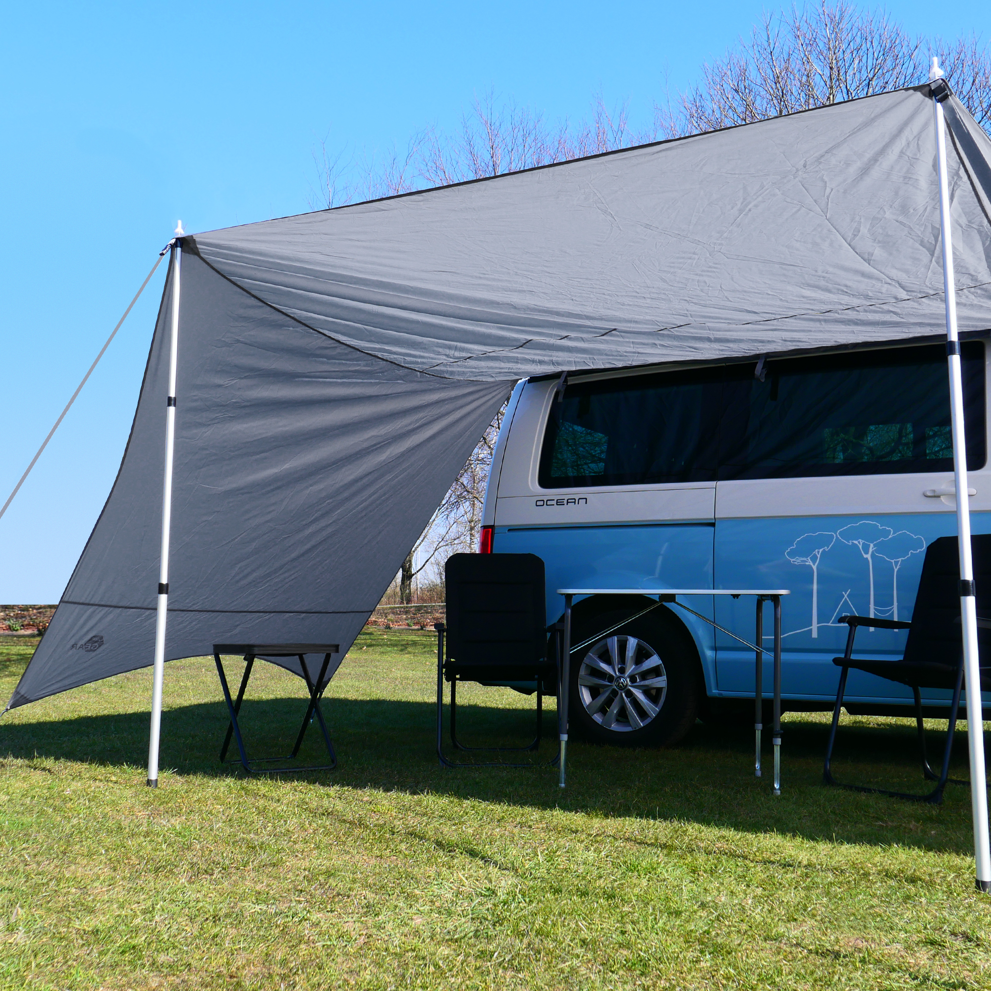 your GEAR Tropea Bus awning UV 50+ in cool gray with two side walls, set up on a blue camper van. Includes aluminum poles, provides sun and rain protection, shown with camping chairs and table underneath.