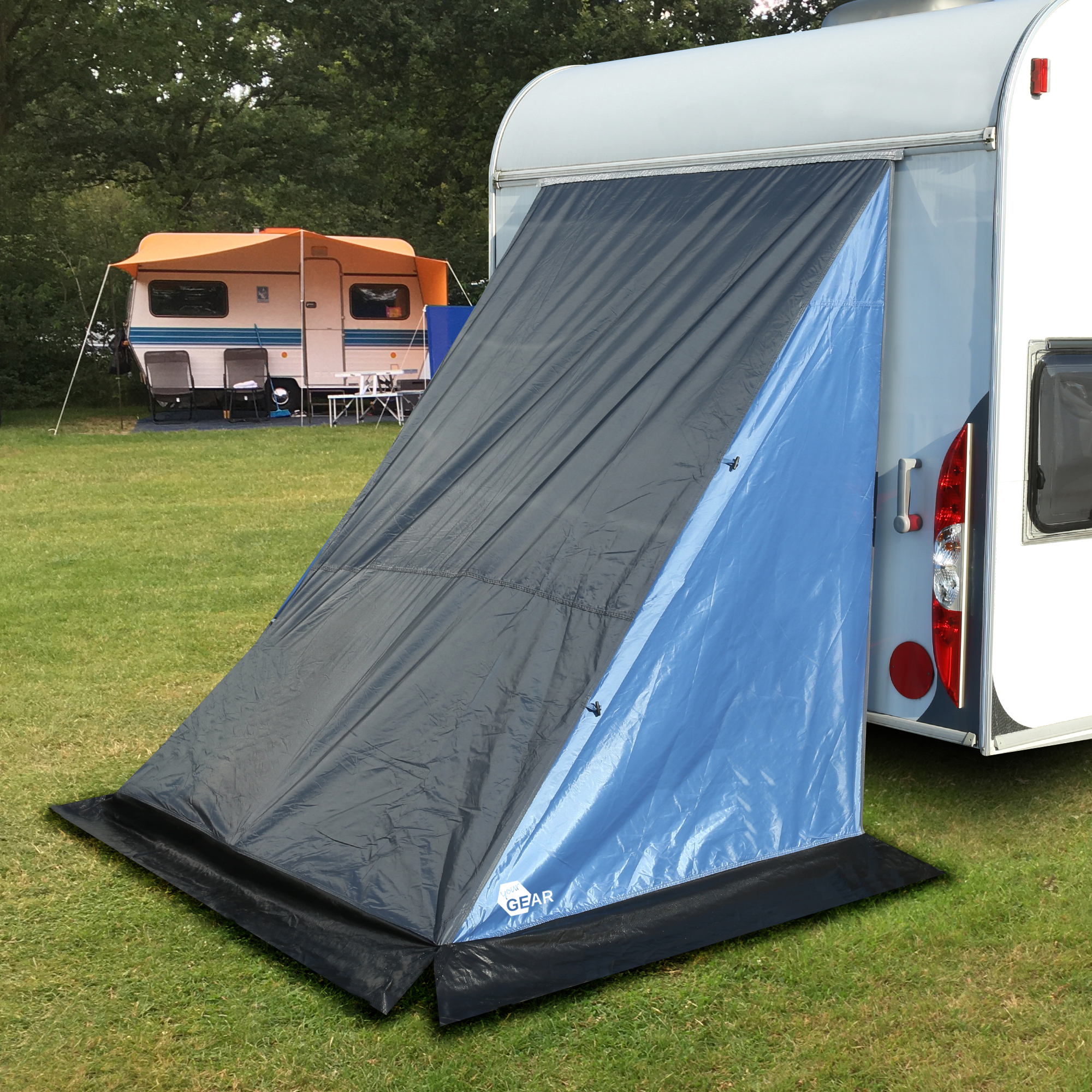your GEAR Adria 140 Caravan Heckzelt als Stauraumzelt, in Blau und Grau, am Heck eines Wohnwagens montiert. Wettergeschütztes Geräte- oder Lagerzelt mit Bodenstreifen auf grüner Wiese.