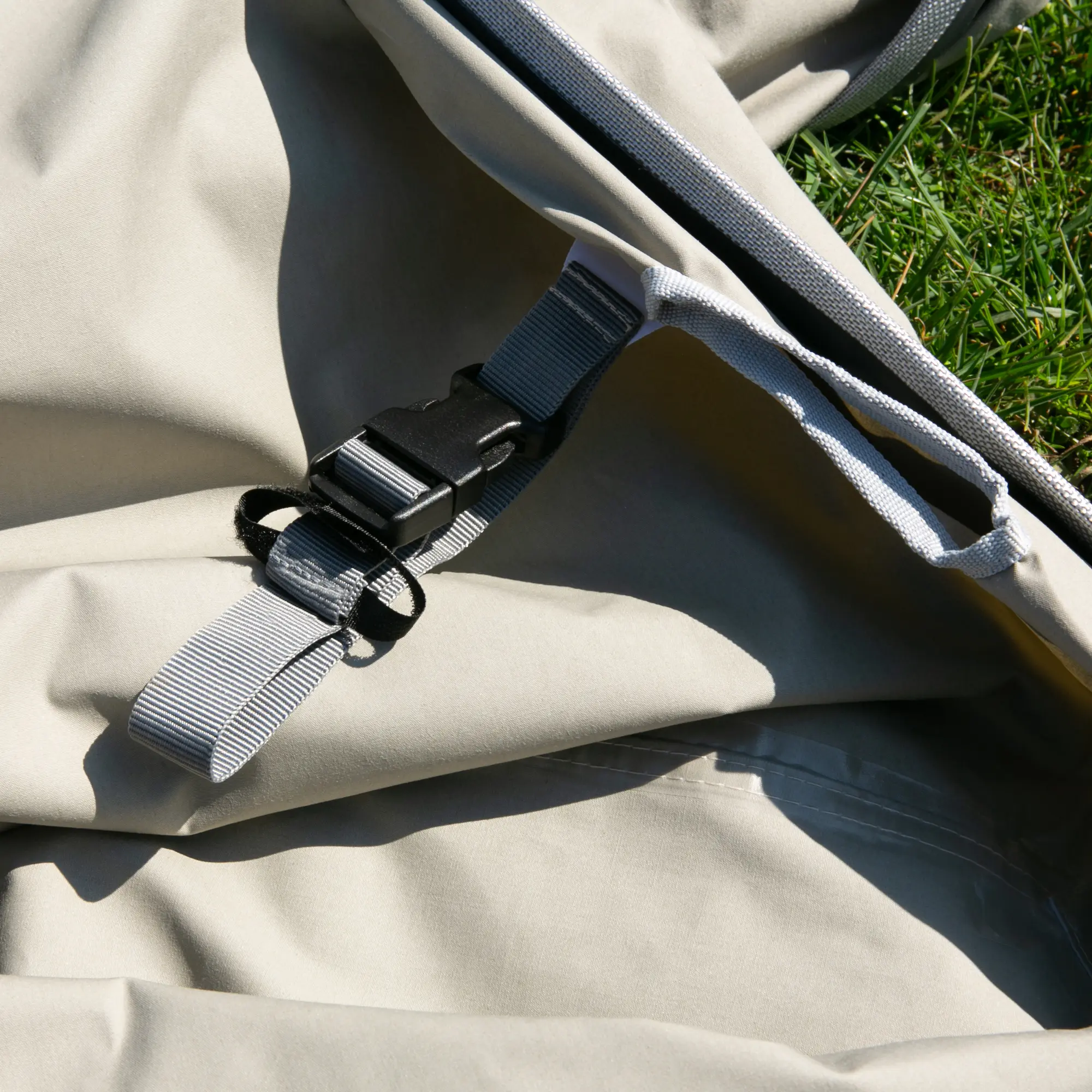 Détail du your GEAR Tropea TC Tarp en toile coton beige, avec sangle de fixation robuste et boucle, posé sur l’herbe. Protection solaire UV 50+ pour bus, van ou camping-car.