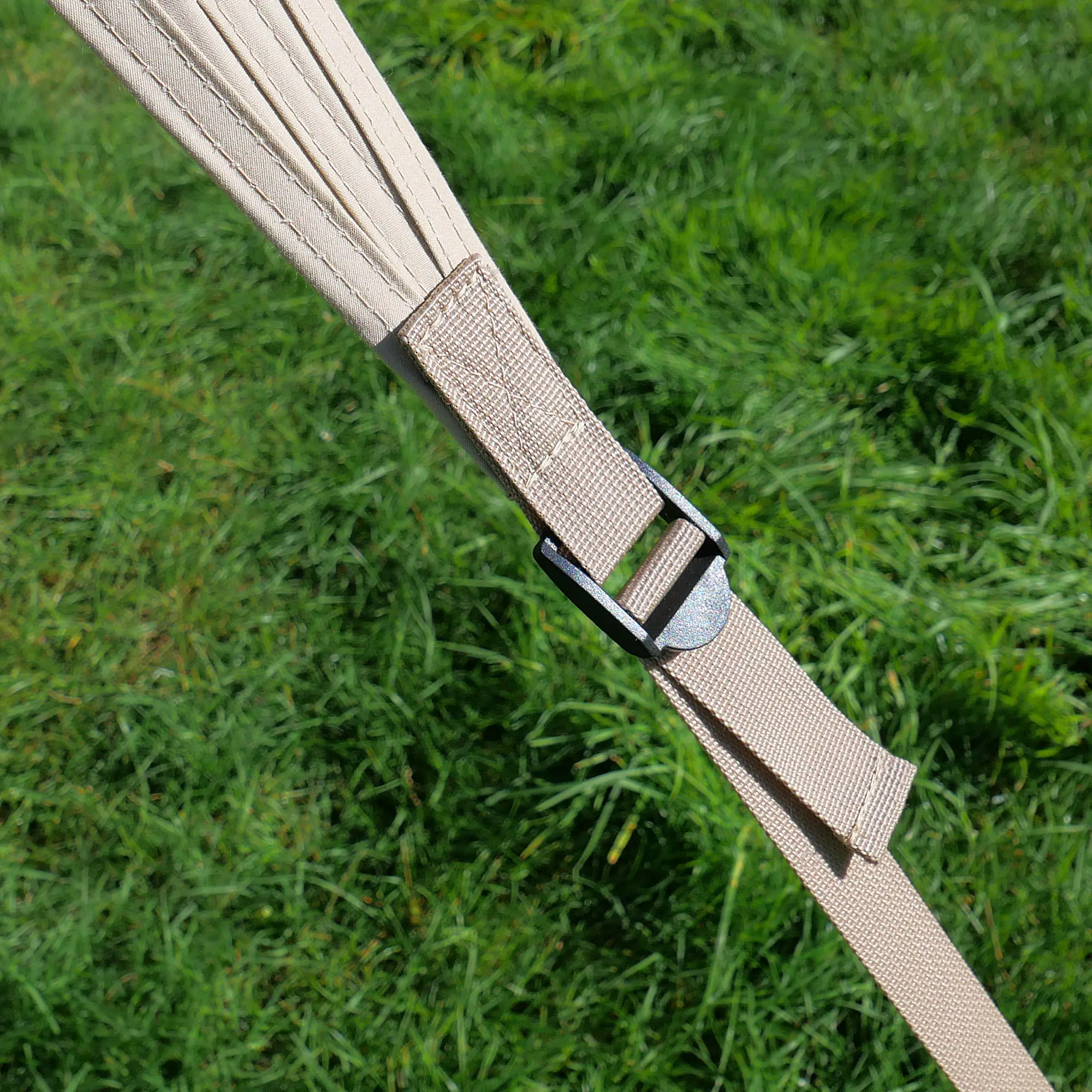 Nahaufnahme eines Befestigungsriemens mit Metallschnalle am your GEAR Scilla TC Caravan Tarp Sonnensegel aus beigem, robustem Gewebe vor grünem Gras. Ideal für Wohnwagen-Sonnenschutz und einfache Montage.
