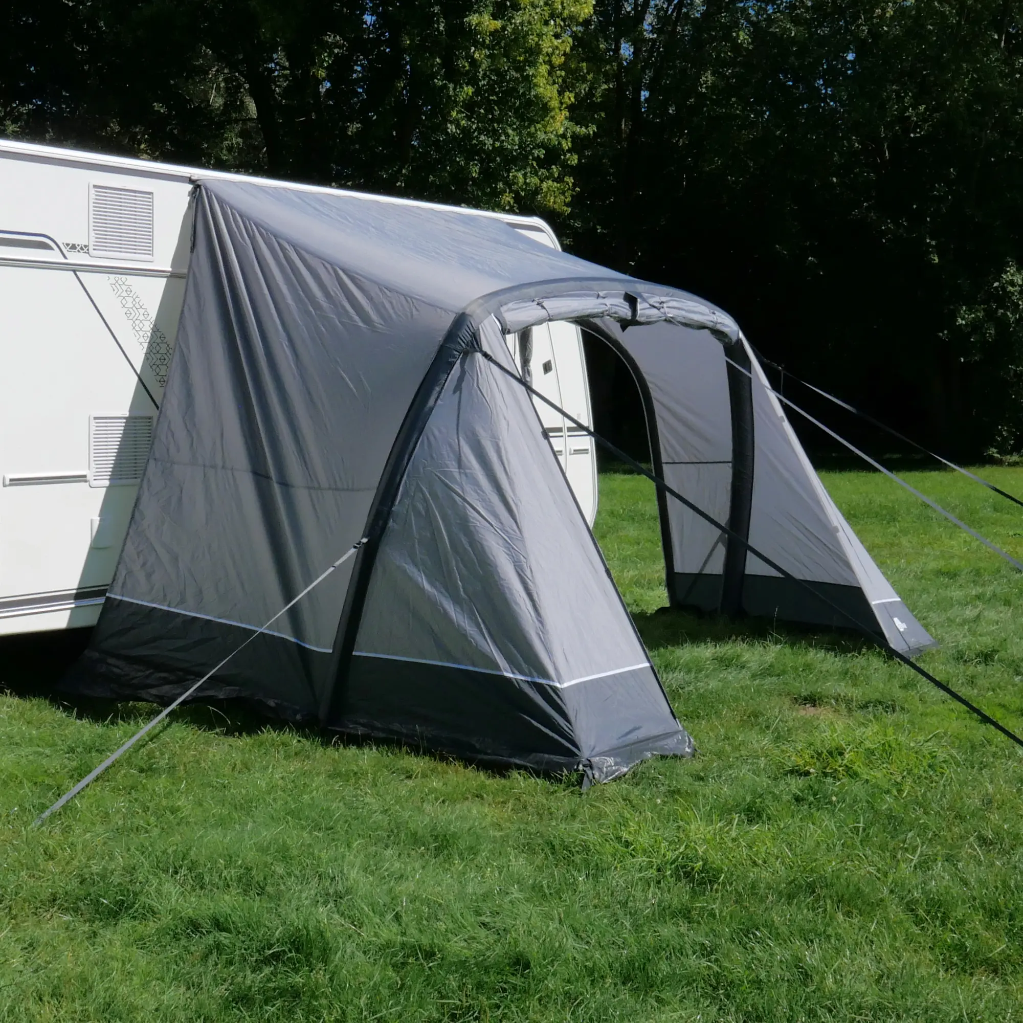 your GEAR Vicenza 350E AIR inflatable caravan awning, 350x250 cm, attached to a white caravan; single air tube frame, grey fabric, large entrance, pitched on grass, ideal for camping and sun protection.