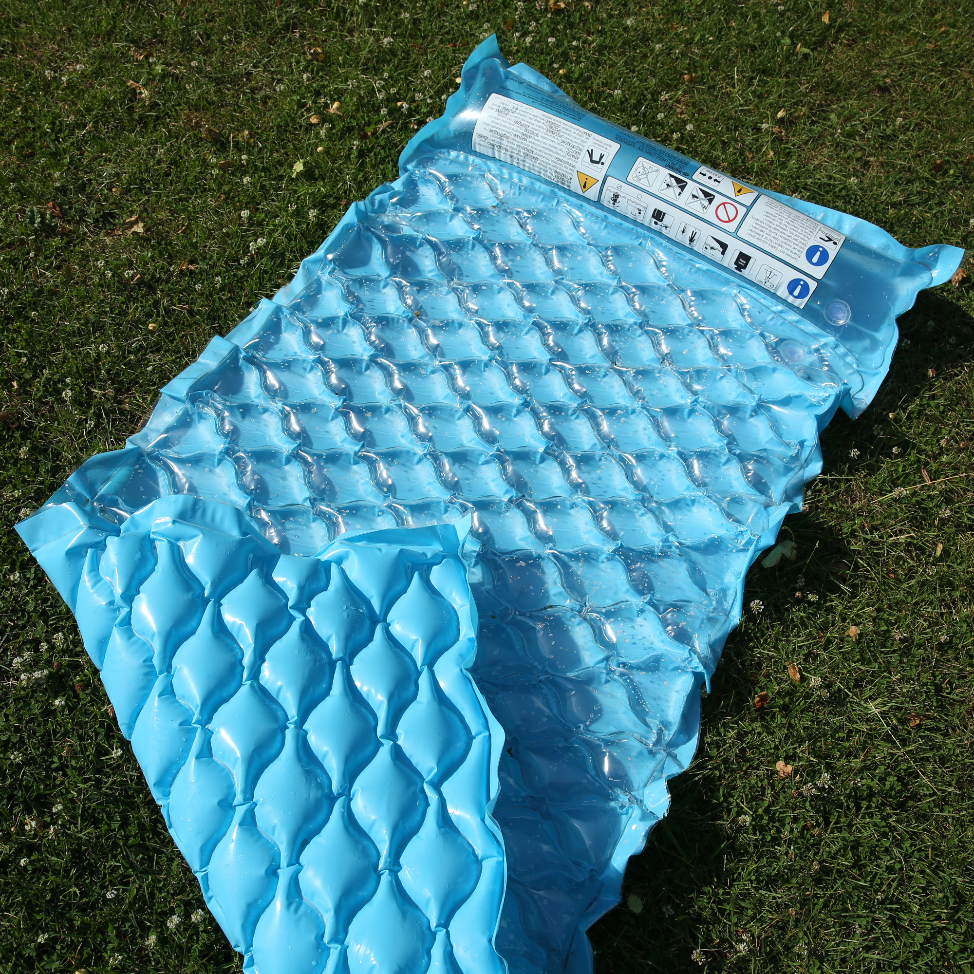 Matelas flottant bleu Jilong Wave Mat 218x88 cm avec structure gaufrée, oreiller intégré et surface confortable, posé sur l’herbe, idéal pour piscine, plage ou lac.