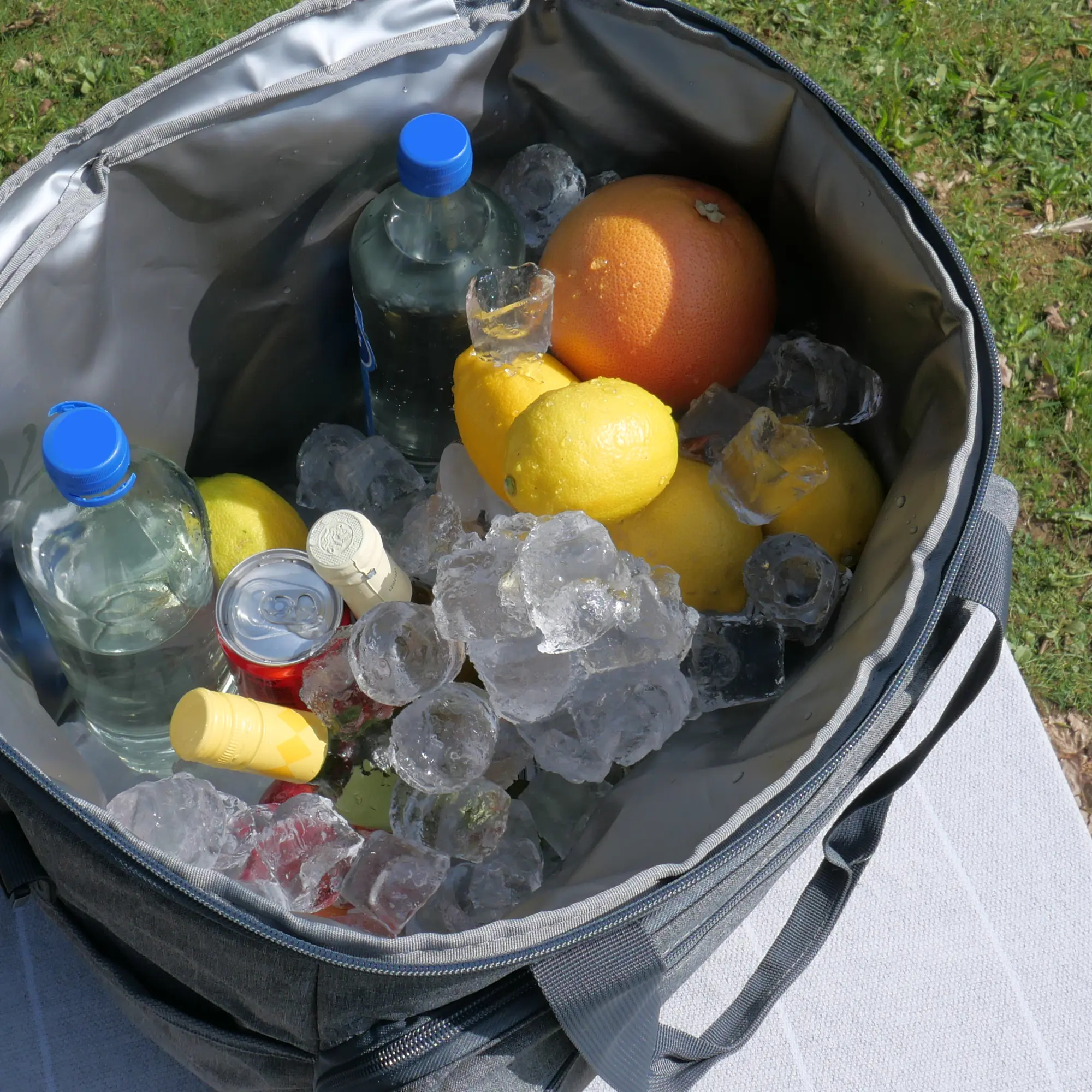 your GEAR foldable cooler bag Cavoli, 30L, shown open outdoors with bottles, fruit, cans, and ice inside; features grey insulated, waterproof lining and sturdy handles, ideal for picnics and shopping.