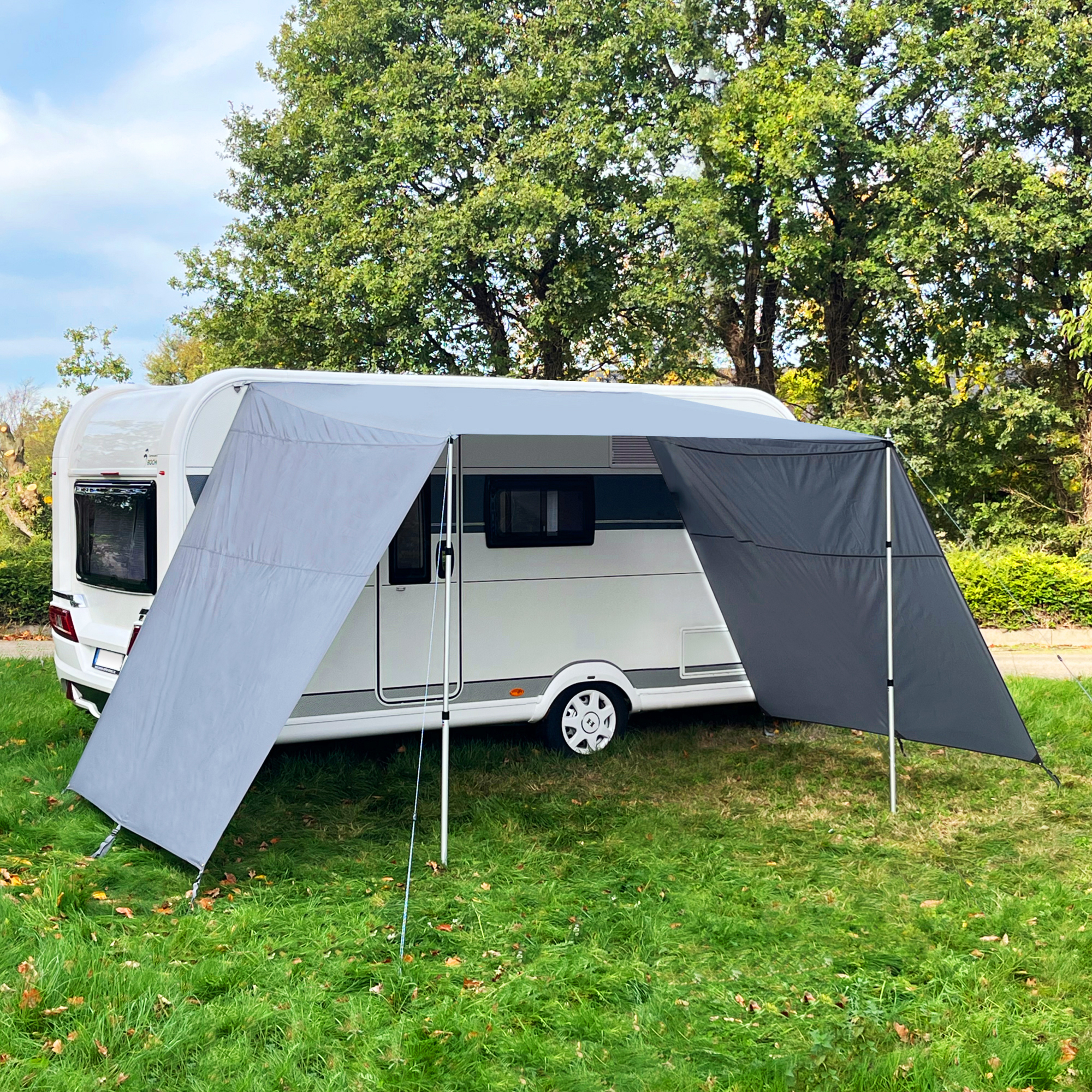Graues your GEAR Teramo 250 Sonnendach mit Seitenwänden am Wohnwagen, gespannt mit Aluminium-Teleskopstangen, bietet UV 50+ Schutz und Wetterschutz auf einer Wiese vor grünem Hintergrund.