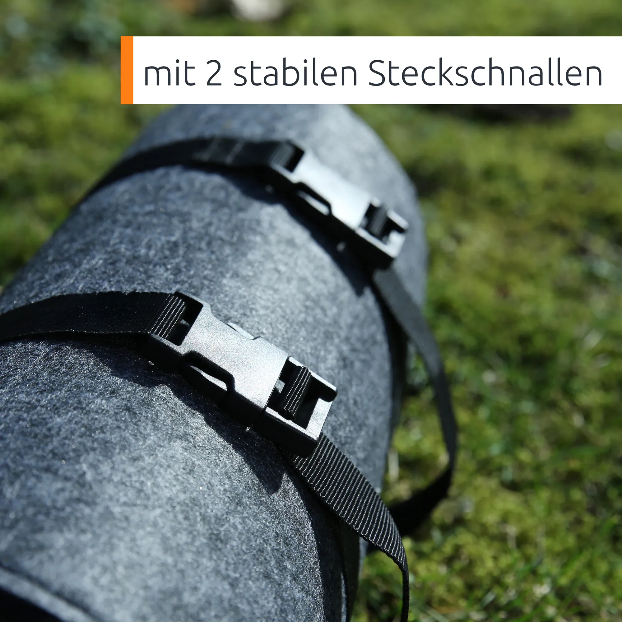 Tapis roulé gris avec deux sangles noires et boucles à clip, posé sur l'herbe.