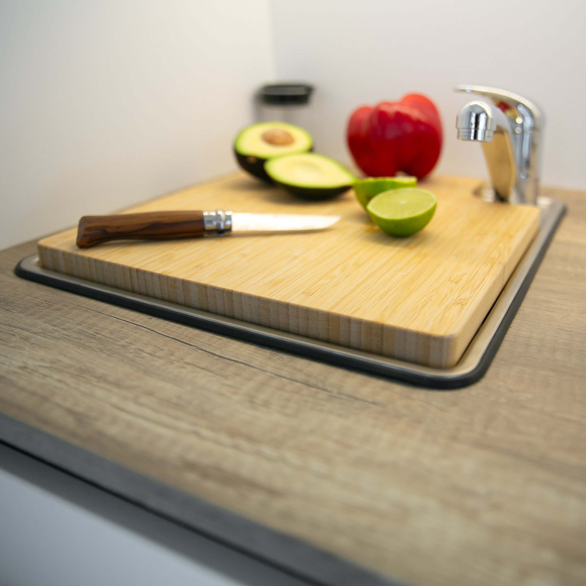 Planche à découper et couvercle d’évier en bambou your GEAR Burano, installés sur un évier de caravane, avec couteau, avocat, citron vert et poivron, parfait pour optimiser l’espace cuisine en camping-car.
