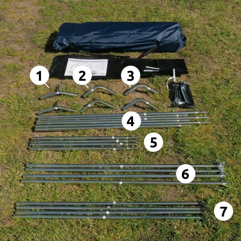 Ensemble complet de pièces pour le your GEAR Trient Multi Storage, incluant tubes métalliques numérotés, connecteurs, piquets, sac de transport et notice, posé sur l’herbe pour montage du tente cuisine 240x180x200 cm.