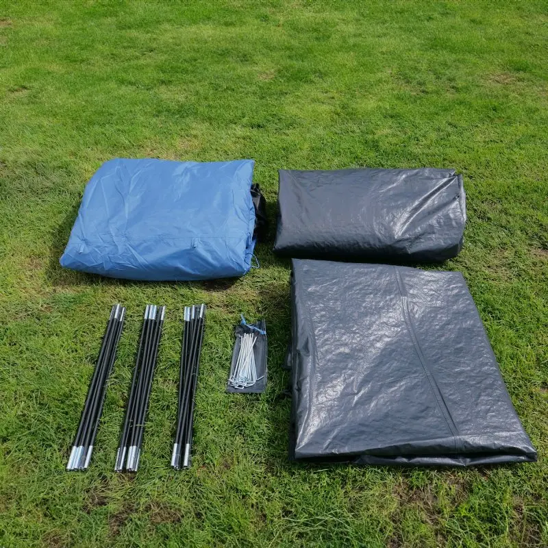 Éléments du your GEAR Zelt Mistral 4 personnes : toiles de tente bleue et noire, arceaux en fibre de verre, piquets en métal, posés sur l’herbe, prêts pour le montage du tunnel familial.