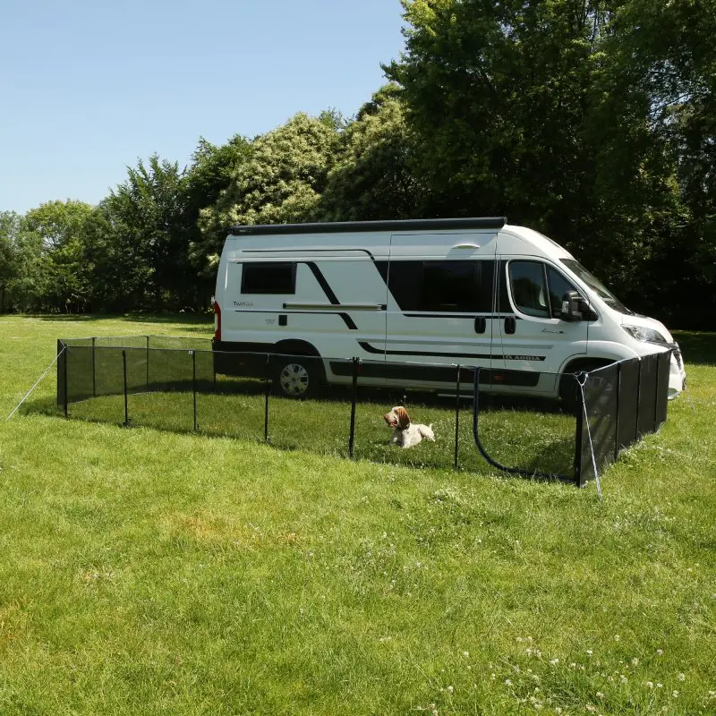 Mobiler Hundezaun your GEAR Larino, 90 cm hoch, als Freigehege neben einem Wohnmobil aufgestellt, mit Mesh-Elementen und Türe, ideal für Camping und Garten, erweiterbar, Hund im Gehege auf grüner Wiese.