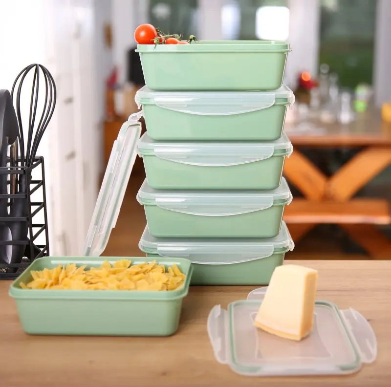 Set di 6 contenitori your GEAR Pila da 1350 ml impilati, in plastica verde con coperchi trasparenti, ideali per alimenti. Un contenitore aperto mostra pasta e formaggio su un coperchio accanto.