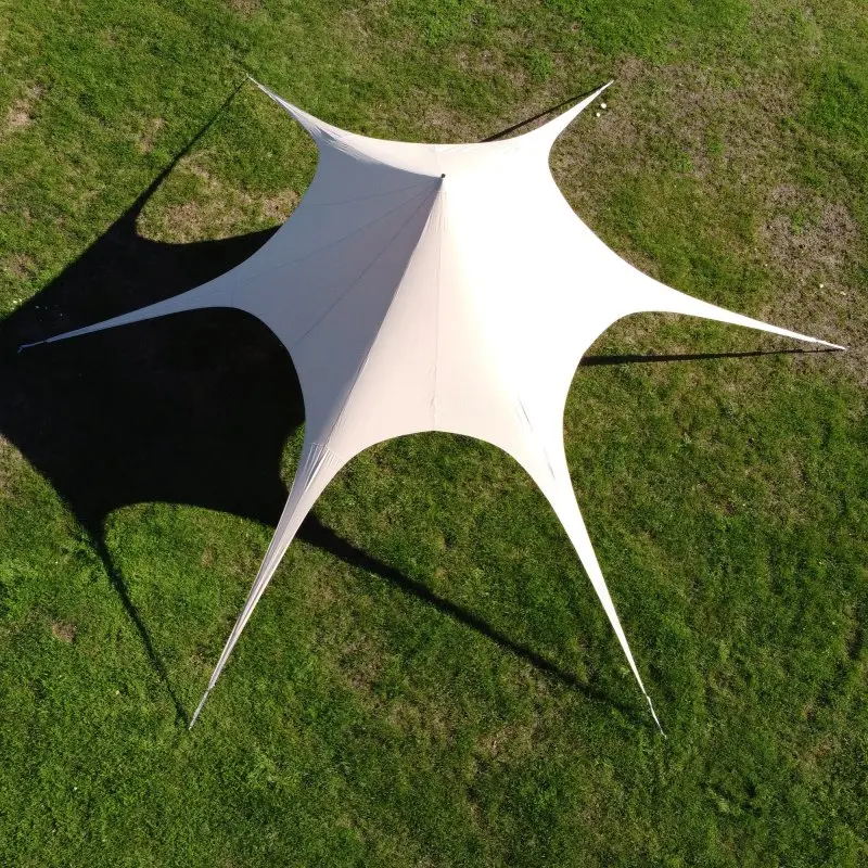 Tente étoile your GEAR Sonora de 10 m de diamètre, en tissu coton mélangé beige, vue du dessus, six points d’ancrage, structure pyramidale sur pelouse, idéale pour l’ombre et la protection extérieure.
