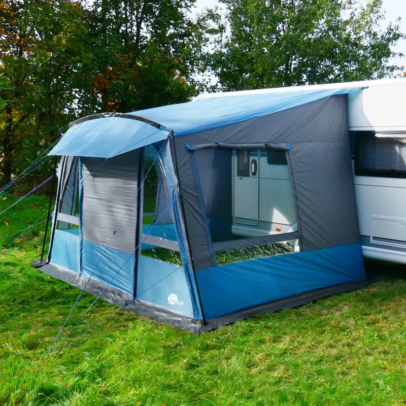your GEAR Malibu 350 caravan awning attached to a white caravan, featuring blue and grey fabric, large clear windows, a sloped roof, and removable front panel, set up on grass with trees in the background.